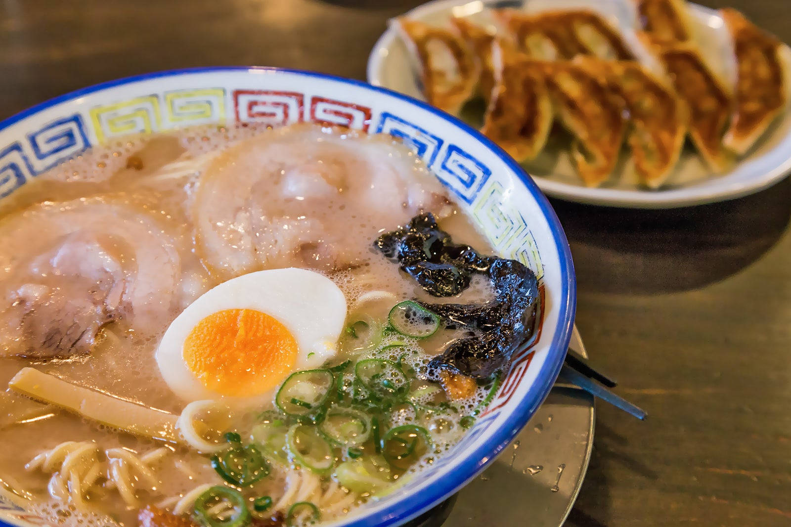 Ramen 桌布 壁紙 — 一碗冒著熱氣的拉麵，配上溏心蛋、青蔥和叉燒，旁邊放著一碟金黃色的煎餃。