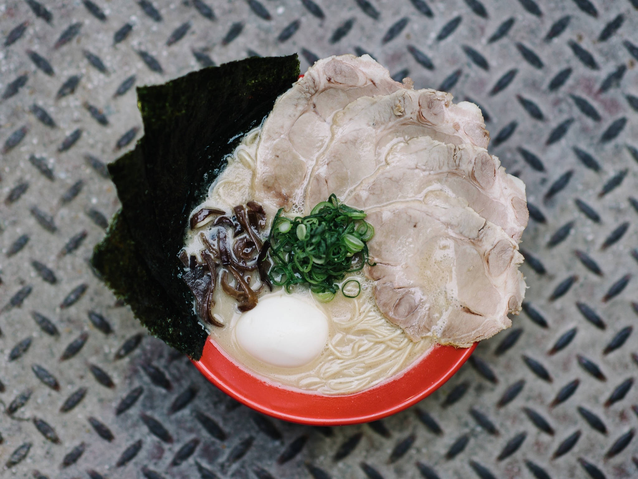 Garlic 桌布 壁紙 — 一碗冒著熱氣的拉麵，配有叉燒豬肉、青蔥和海苔，放在有紋理的金屬表面上。