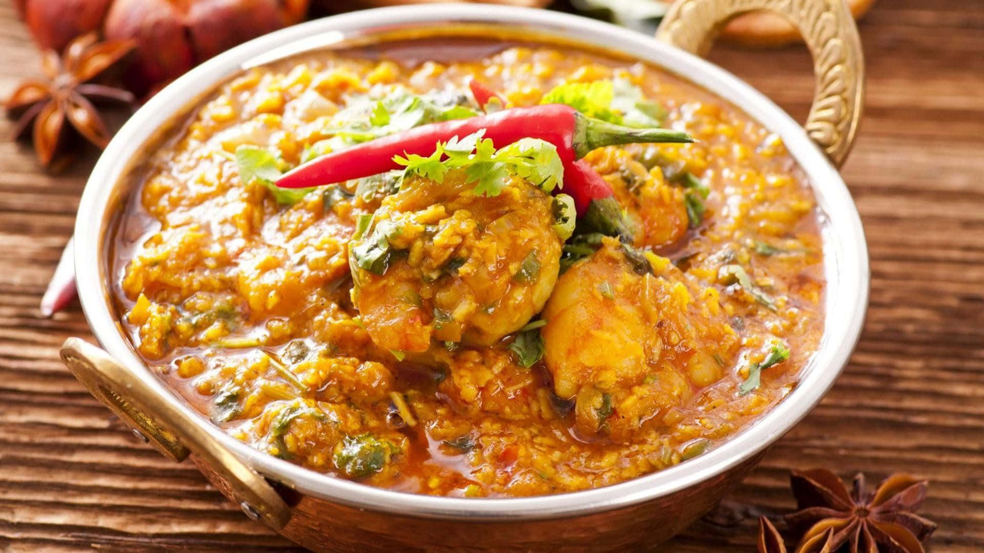 Indian Food 桌布 壁紙 — 一碗冒著熱氣的濃郁橙色咖哩雞，飾以紅辣椒和香菜，放在木桌上，旁邊有八角。