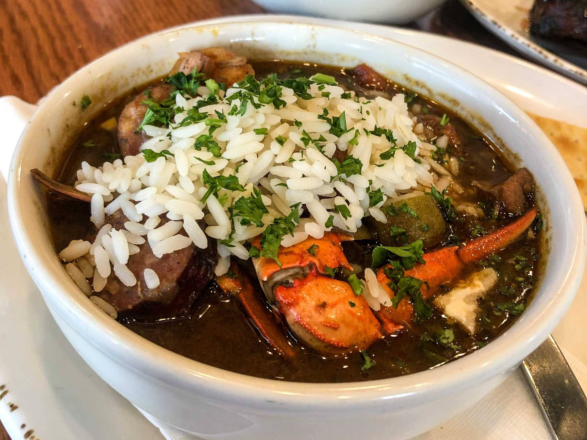 shrimp 桌布 壁紙 — 一碗冒著熱氣的濃郁深色秋葵濃湯，上面鋪著白米飯和新鮮綠色香草，放在木桌上。