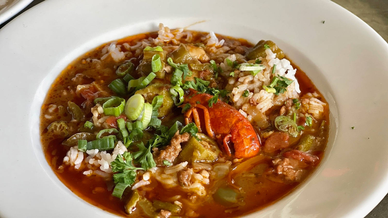 Rice 桌布 壁紙 — 一碗冒著熱氣的濃郁紅色秋葵湯，搭配米飯、青蔥和整條小龍蝦尾，並以新鮮香草點綴。