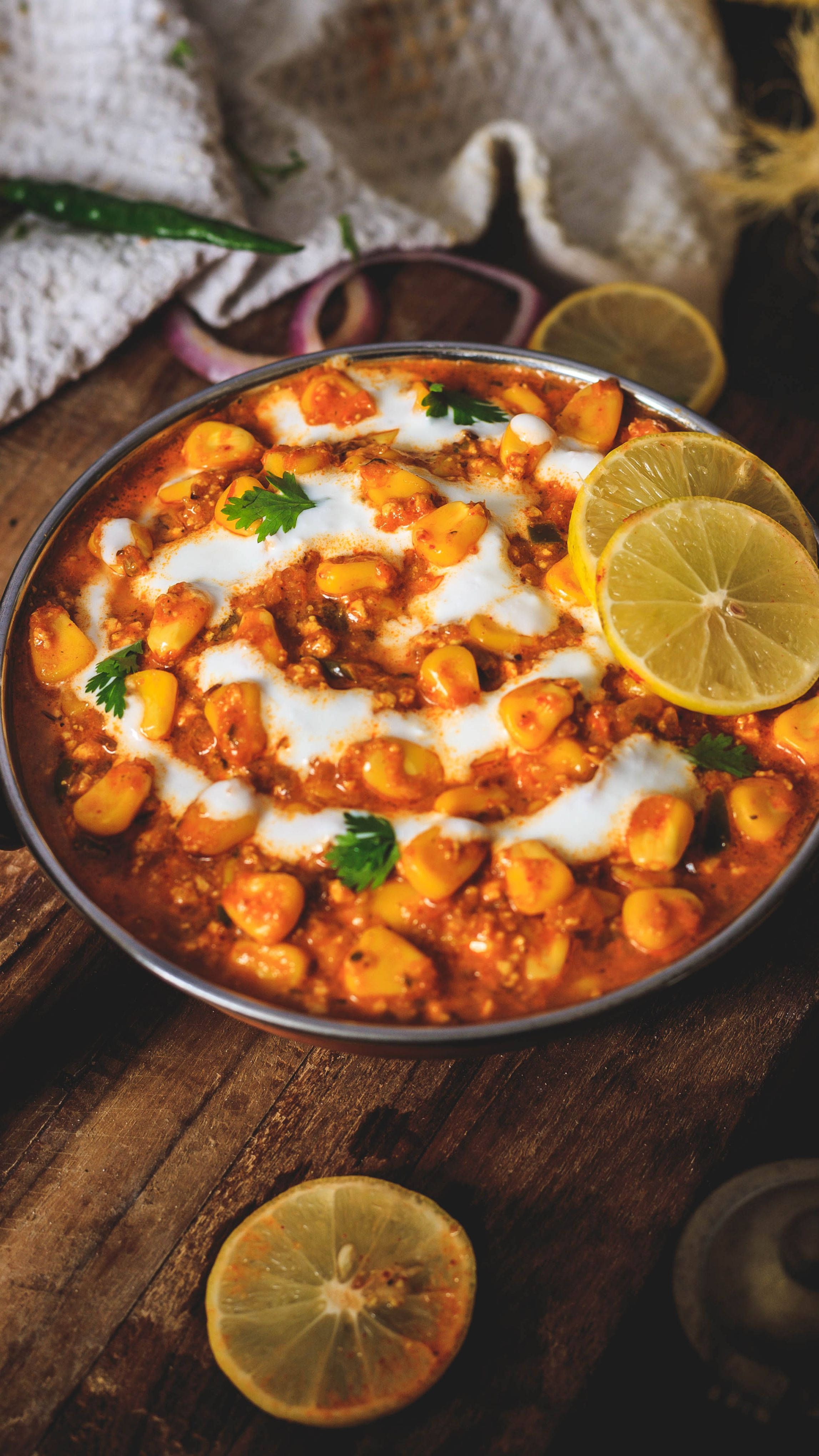 Delicious Food 桌布 壁紙 — 一碗冒著熱氣的鮮橙色chole masala，上面點綴著優格、檸檬片和香菜，放在一張質樸的木桌上。