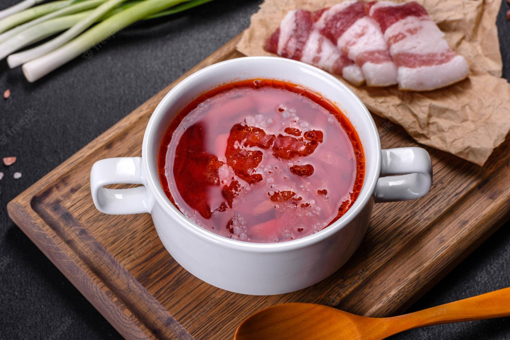 beetroot 桌布 壁紙 — 一碗冒著熱氣的鮮紅色羅宋湯放在木板上，旁邊有生培根片和青蔥。