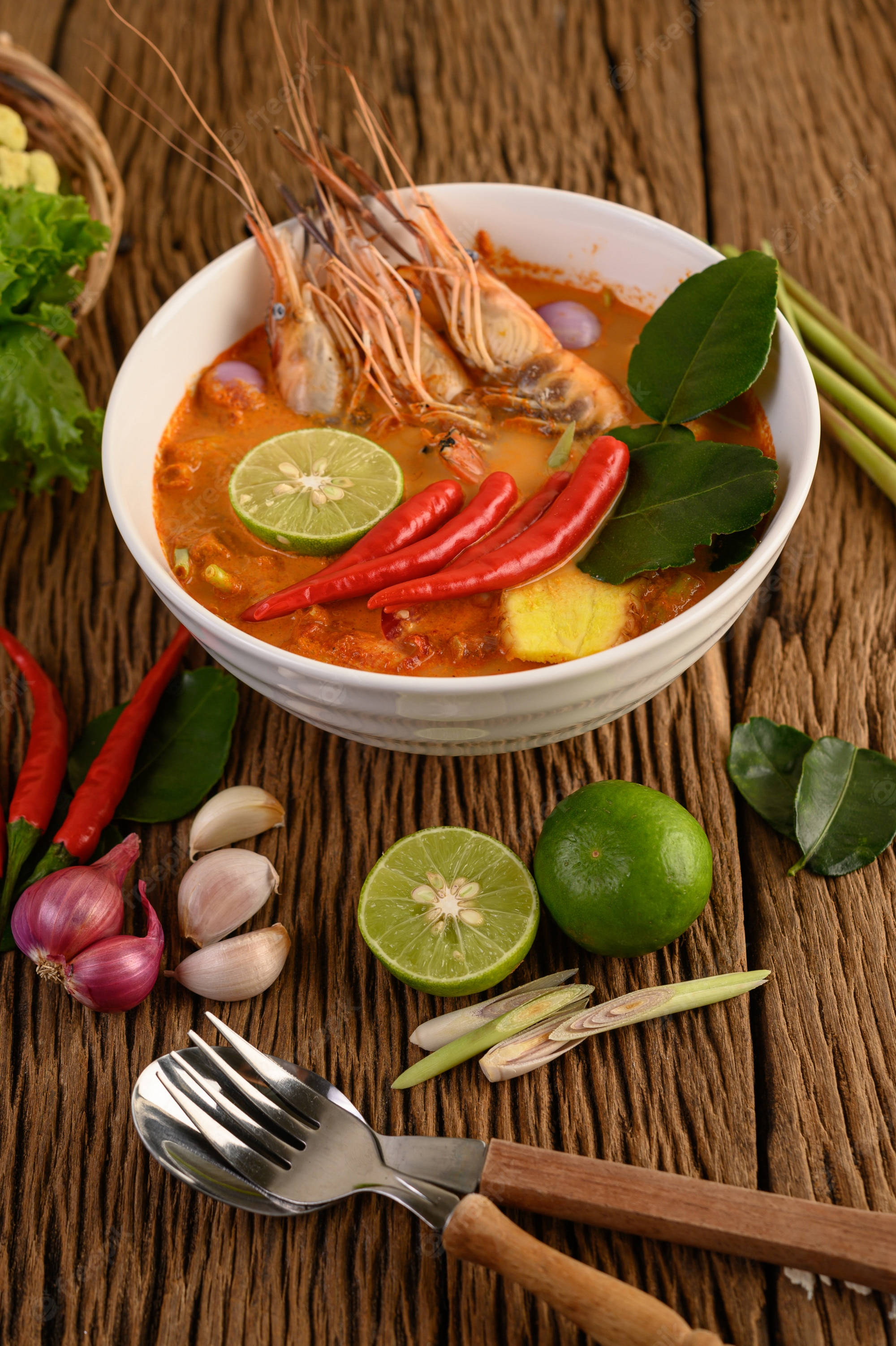 Prawns 桌布 壁紙 — 一碗冒著蒸氣的辛辣泰式冬陰功湯，搭配蝦子、青檸和辣椒，放在被新鮮食材環繞的鄉村風格木桌上。