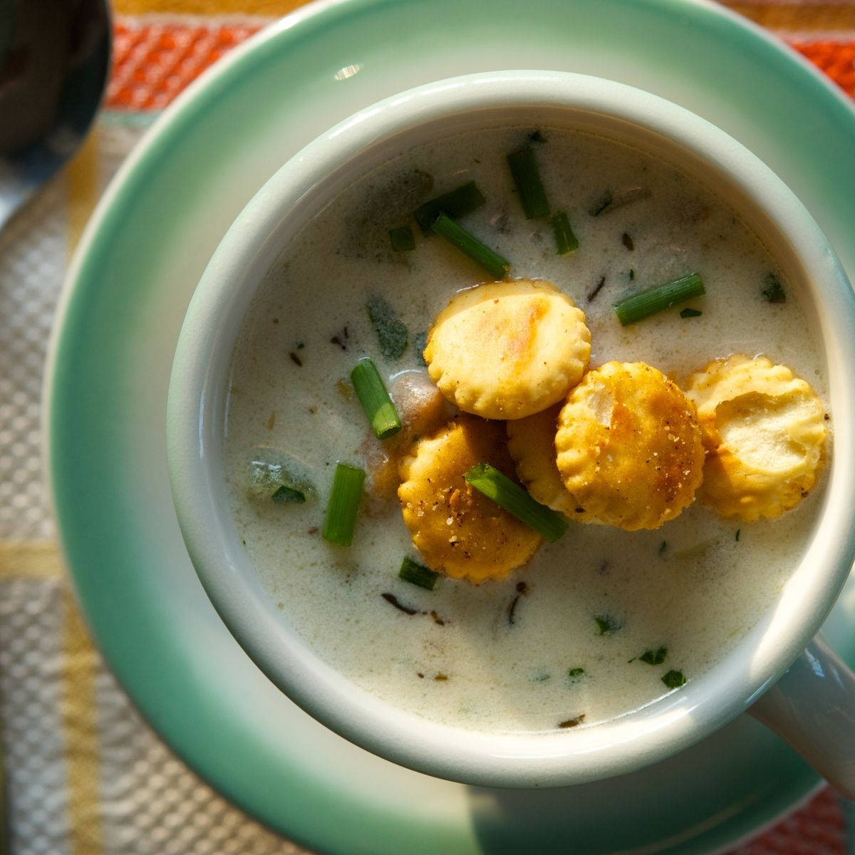 Soup 桌布 壁紙 — 一碗奶油白湯，上面放著金黃色的蠔餅乾和切碎的青蔥，盛在白色馬克杯中，放在青綠色茶托上。