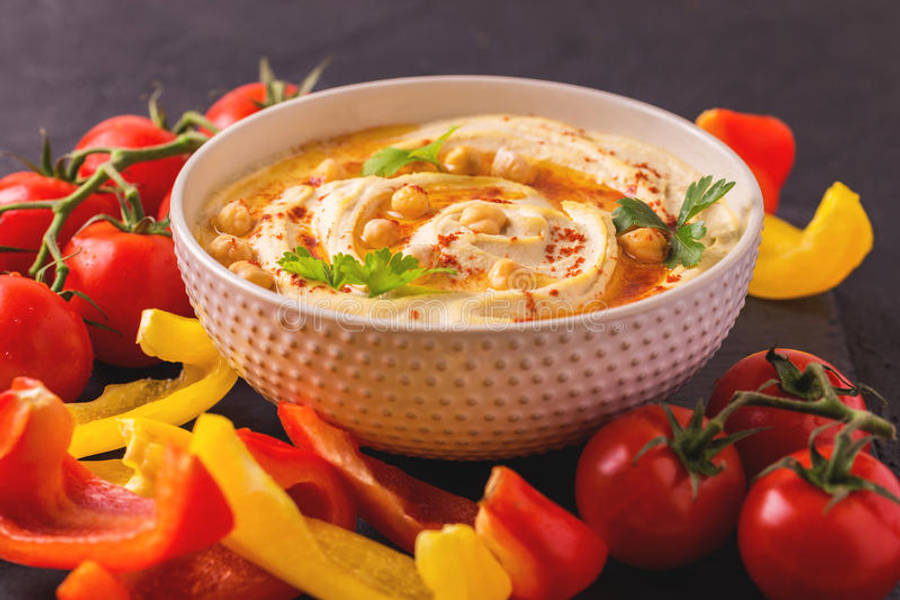 Food Photography 桌布 壁紙 — 一碗奶油般的鷹嘴豆泥，飾以鷹嘴豆、紅椒粉和歐芹，周圍是新鮮番茄和甜椒。