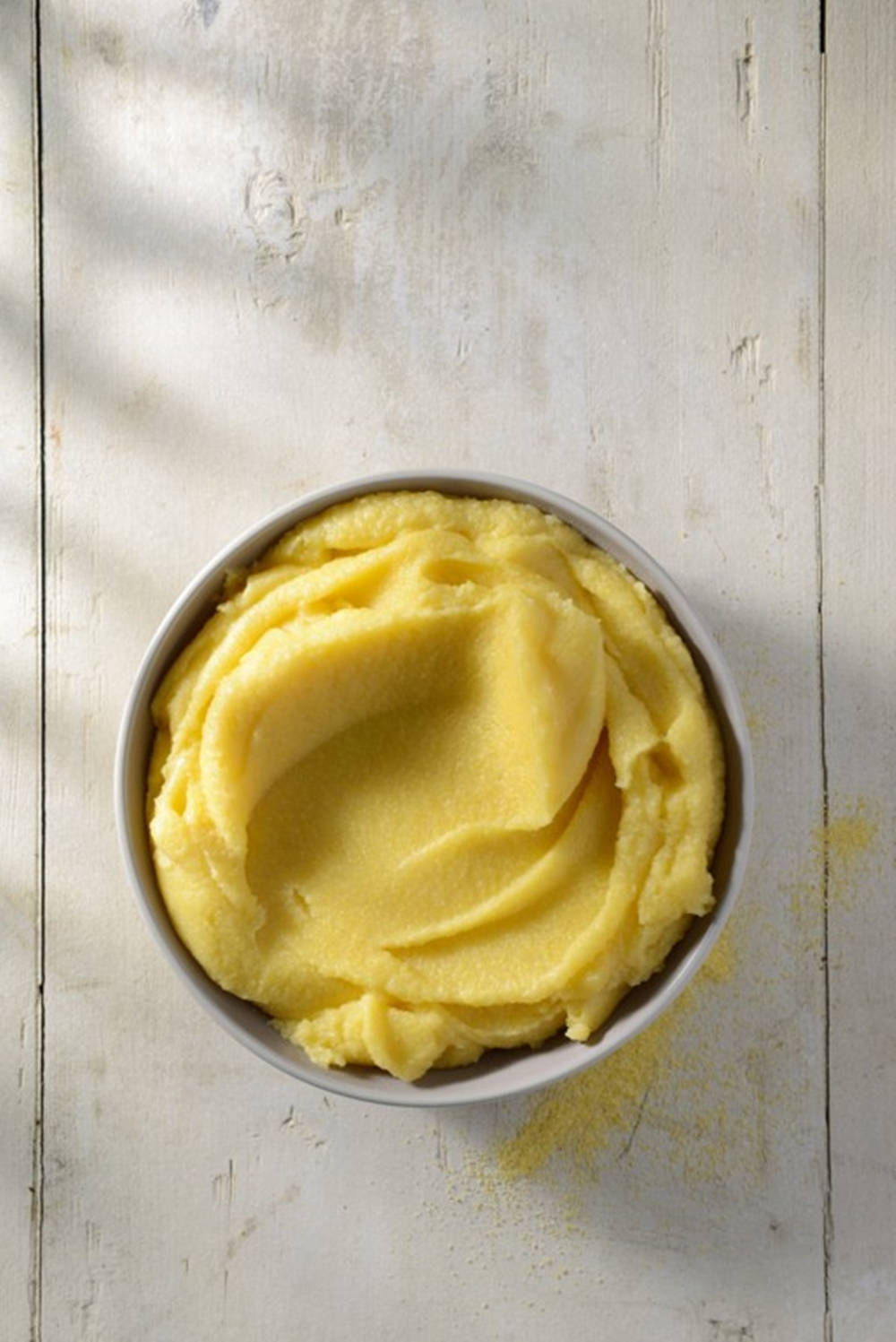 Polenta 桌布 壁紙 — 一碗奶油黃色玉米糊放在經風化的白色木質表面上，柔和自然光投射出陰影。