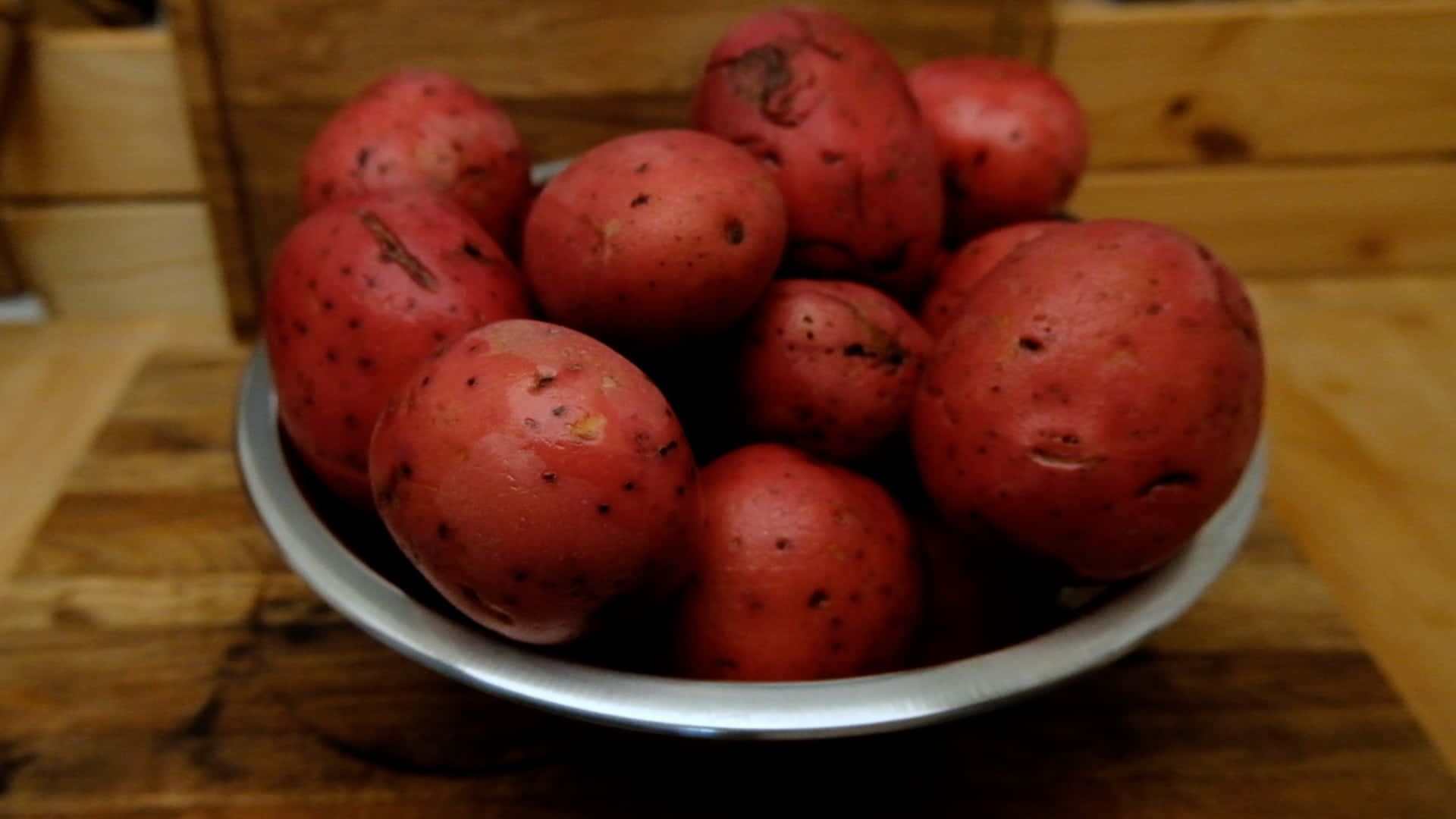 Red Potatoes 桌布 壁紙 — 一碗帶有斑點皮的鮮紅色馬鈴薯放在木質表面上，處於溫暖的室內燈光下。