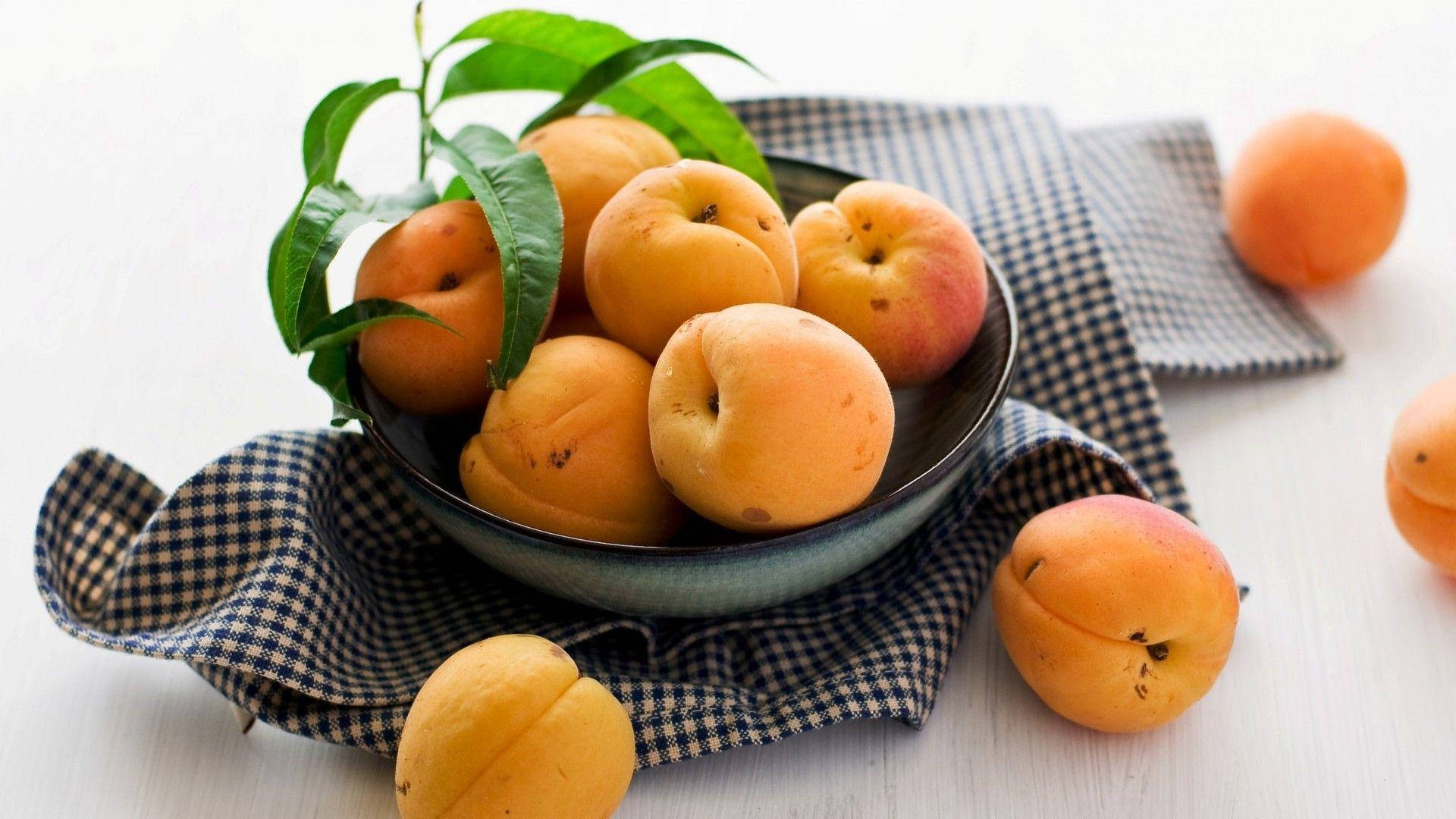 Fruit 桌布 壁紙 — 一碗成熟的杏子配綠葉，放在格子布上，背景為亮白色。