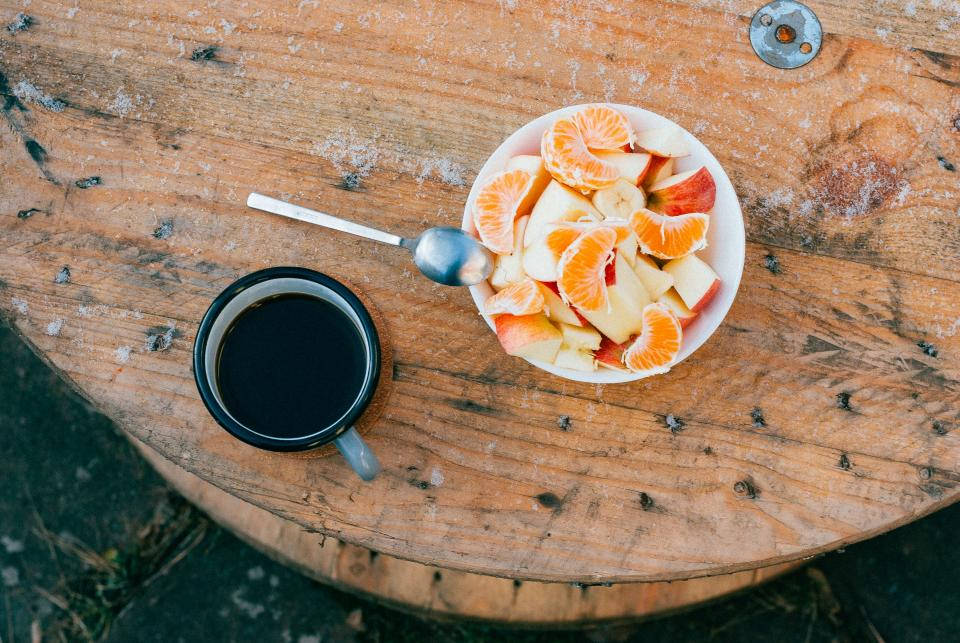 Fruits 桌布 壁紙 — 一碗新鮮水果和一個黑色咖啡杯放在一張風化的木桌上，俯視圖。