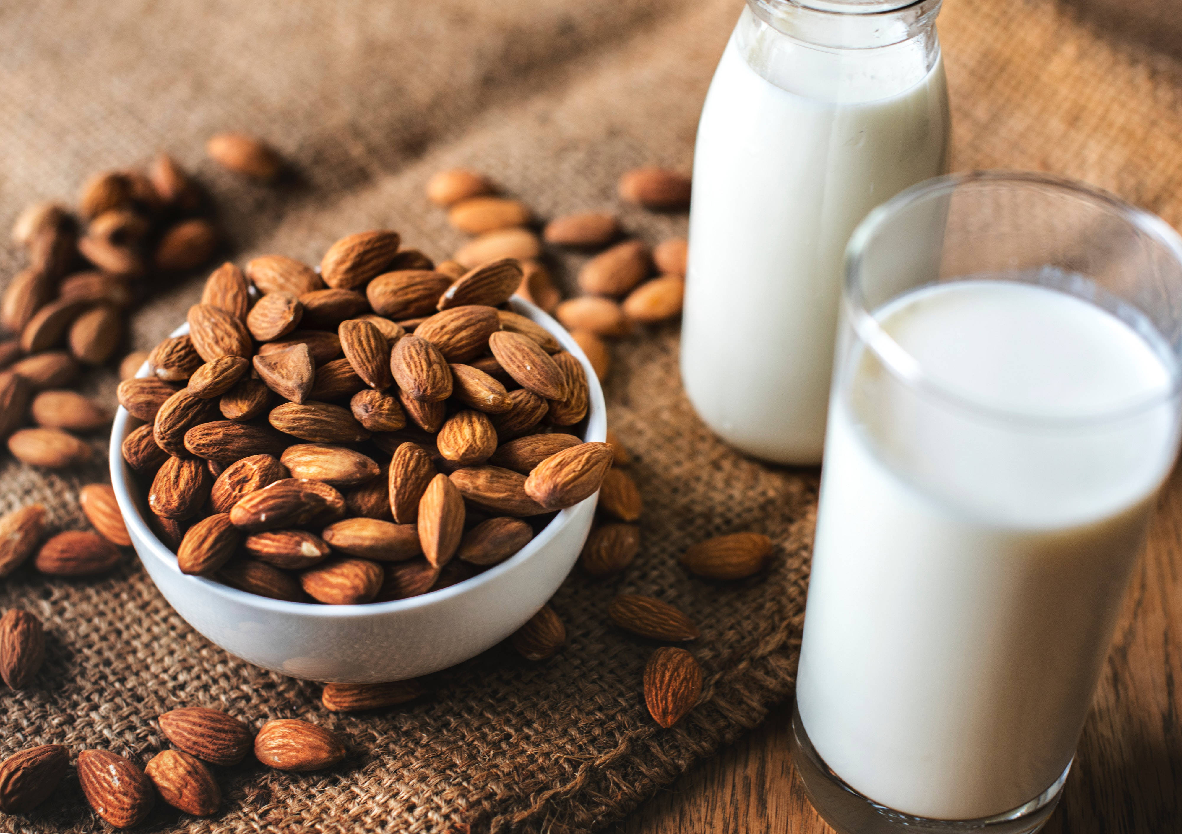 Milk 桌布 壁紙 — 一碗樸素的杏仁放在木頭上的粗麻布上，旁邊有一個玻璃杯和一瓶杏仁奶。