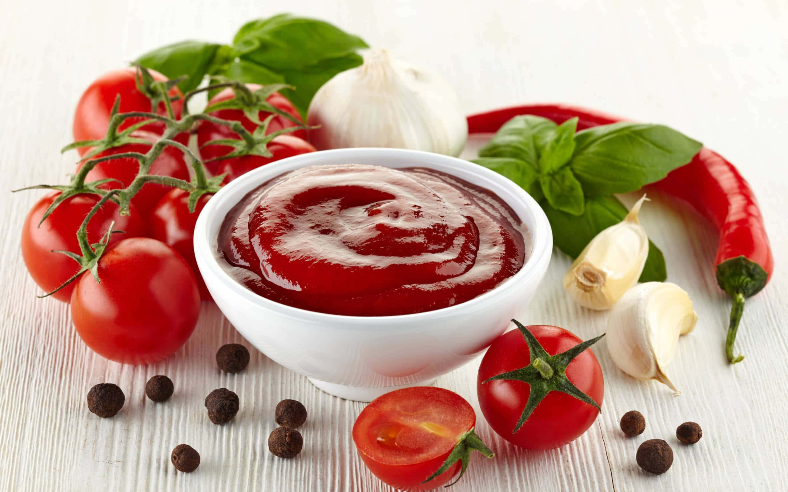 Red Sauce 桌布 壁紙 — 一碗濃郁的紅色番茄醬，周圍是新鮮番茄、羅勒、大蒜和胡椒粒，放在白色木質表面上。