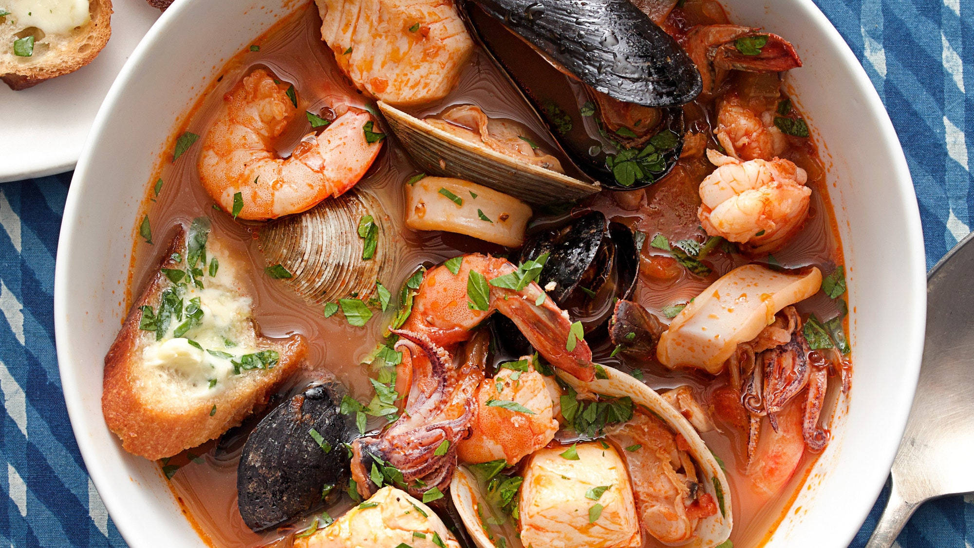Seafood 桌布 壁紙 — 一碗熱氣騰騰的海鮮燉菜，滿是蝦、貽貝、蛤蜊和魷魚，配上新鮮歐芹和奶油麵包。