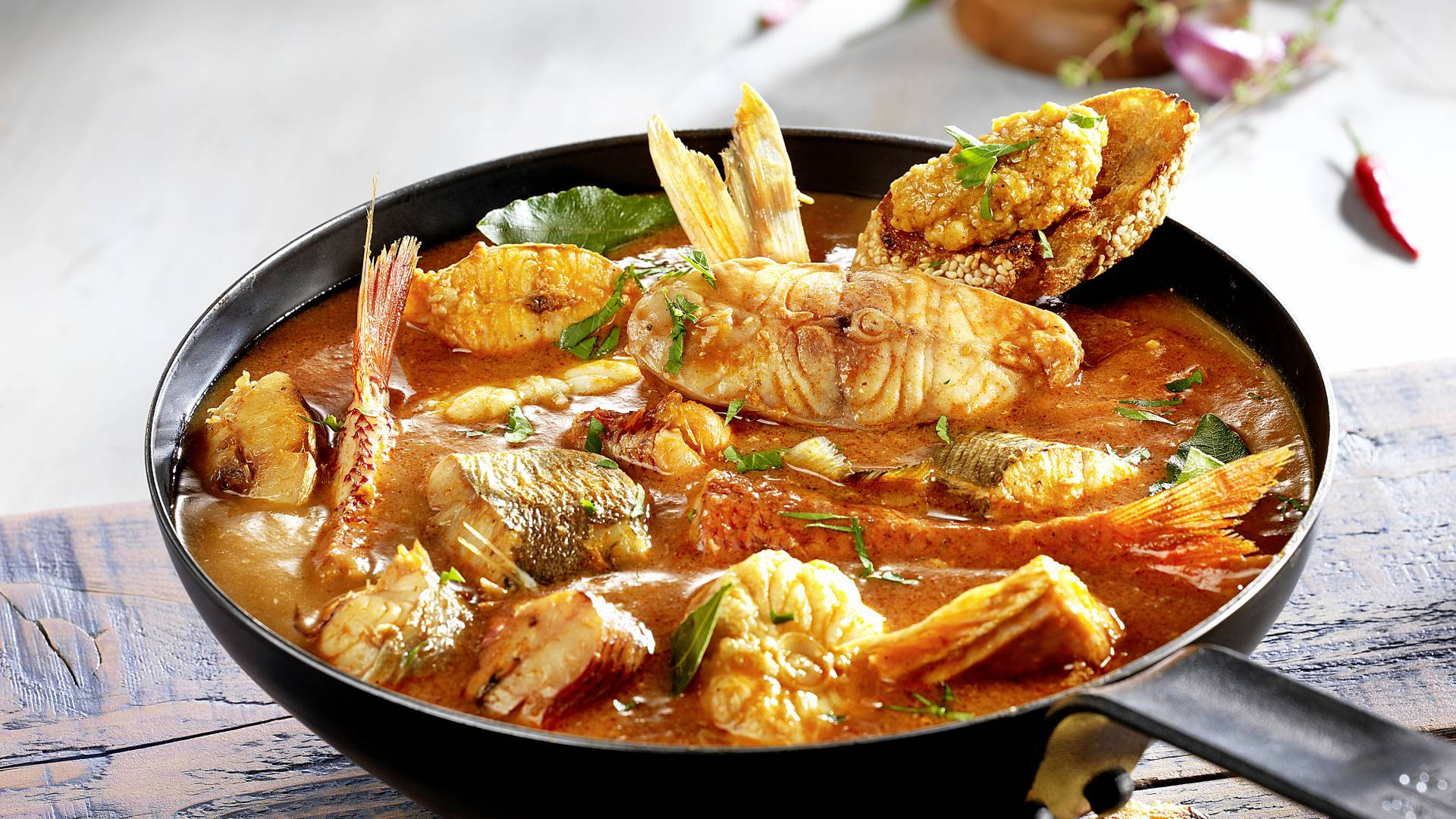 Food Photography 桌布 壁紙 — 一碗熱氣騰騰的濃郁紅咖哩魚，配上整條魚和炸麵包，並以香草點綴，放在質樸的木桌上。