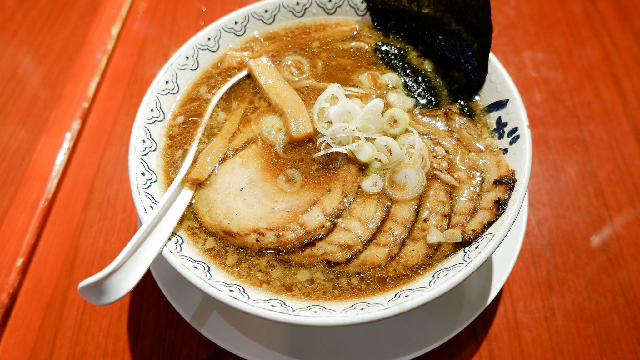 Ramen 桌布 壁紙 — 一碗熱騰騰的拉麵，配上叉燒、青蔥和海苔，放在一張鮮紅色的木桌上。