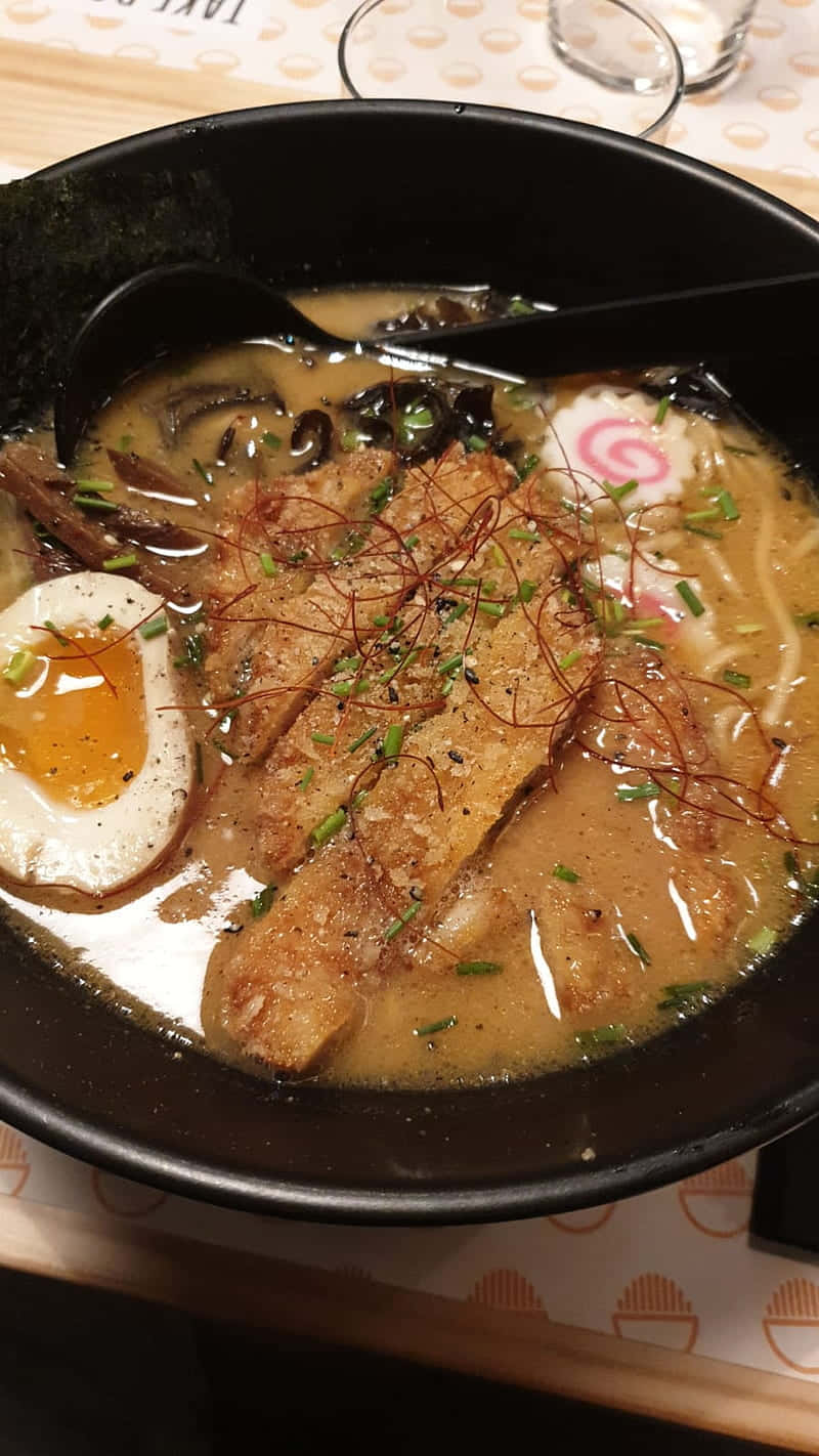 Noodles 桌布 壁紙 — 一碗熱騰騰的拉麵，配有溏心蛋、脆皮叉燒、麵條和青蔥，湯底濃郁。