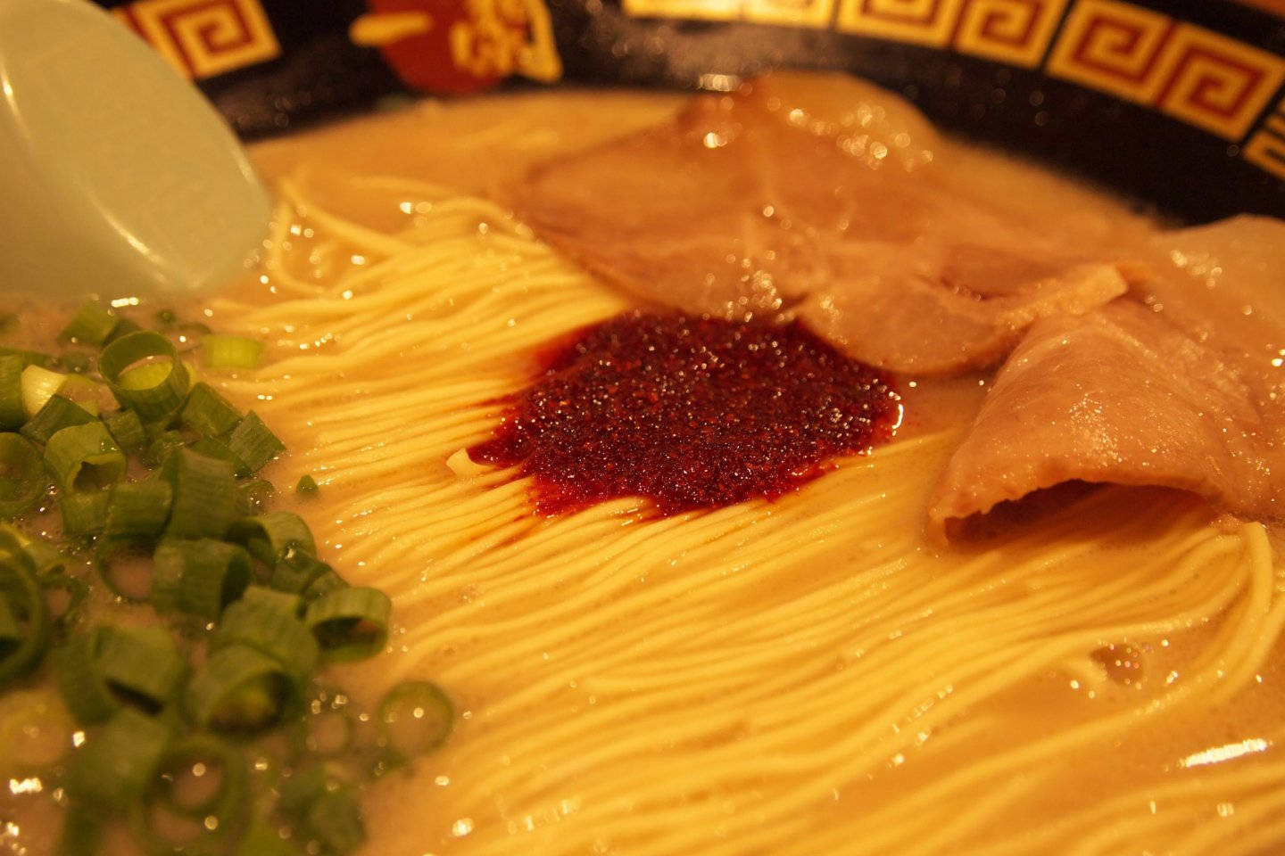 Spicy 桌布 壁紙 — 一碗熱騰騰的拉麵，金黃色的麵條上鋪著叉燒、辣椒油和蔥花。