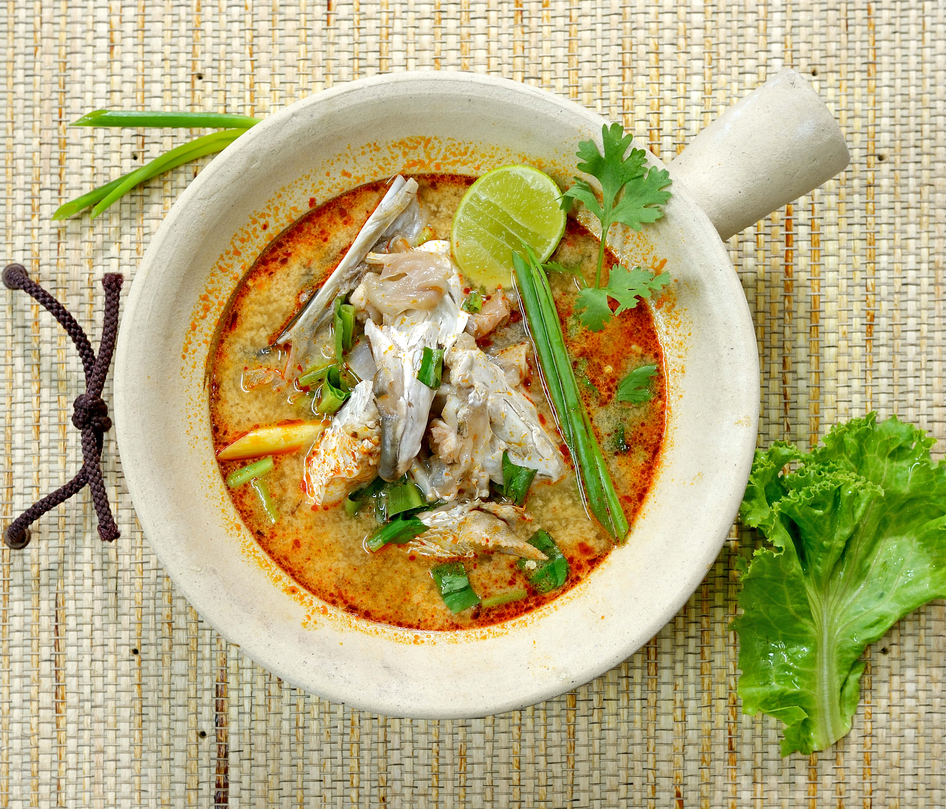 Food Photography 桌布 壁紙 — 一碗熱騰騰的泰式酸辣湯（冬陰功）配魚肉、青檸和香菜，放在編織墊上，旁邊有新鮮生菜。