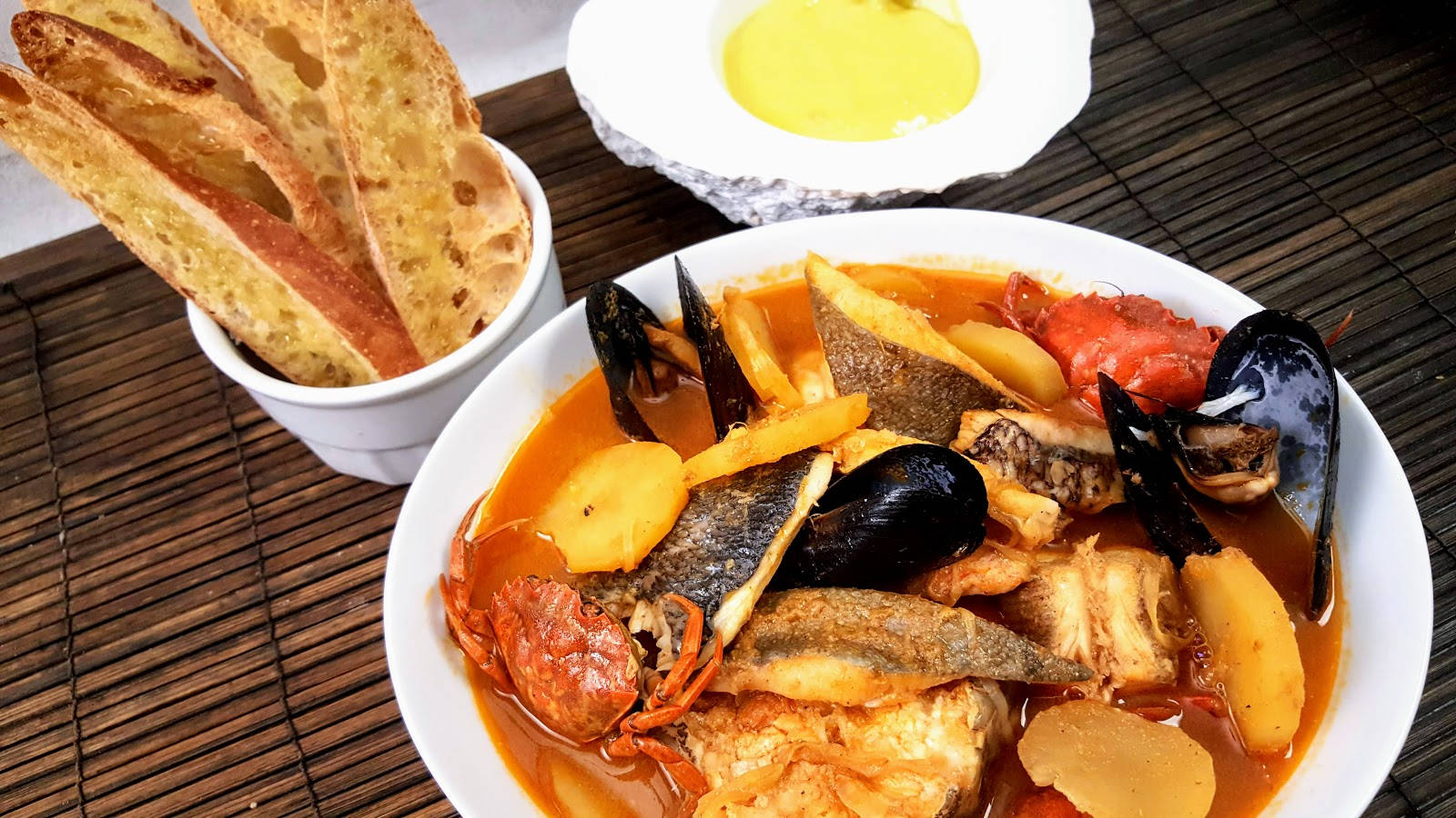 Food Photography 桌布 壁紙 — 一碗熱騰騰的海鮮燉菜，有淡菜、蟹、魚和馬鈴薯，配大蒜麵包，放在竹蓆上。