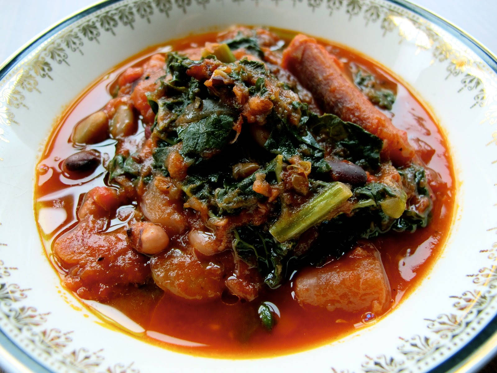 Delicious Food 桌布 壁紙 — 一碗熱騰騰的濃郁番茄燉菜，搭配綠葉蔬菜、豆類和香腸，盛在帶圖案的陶瓷盤中。