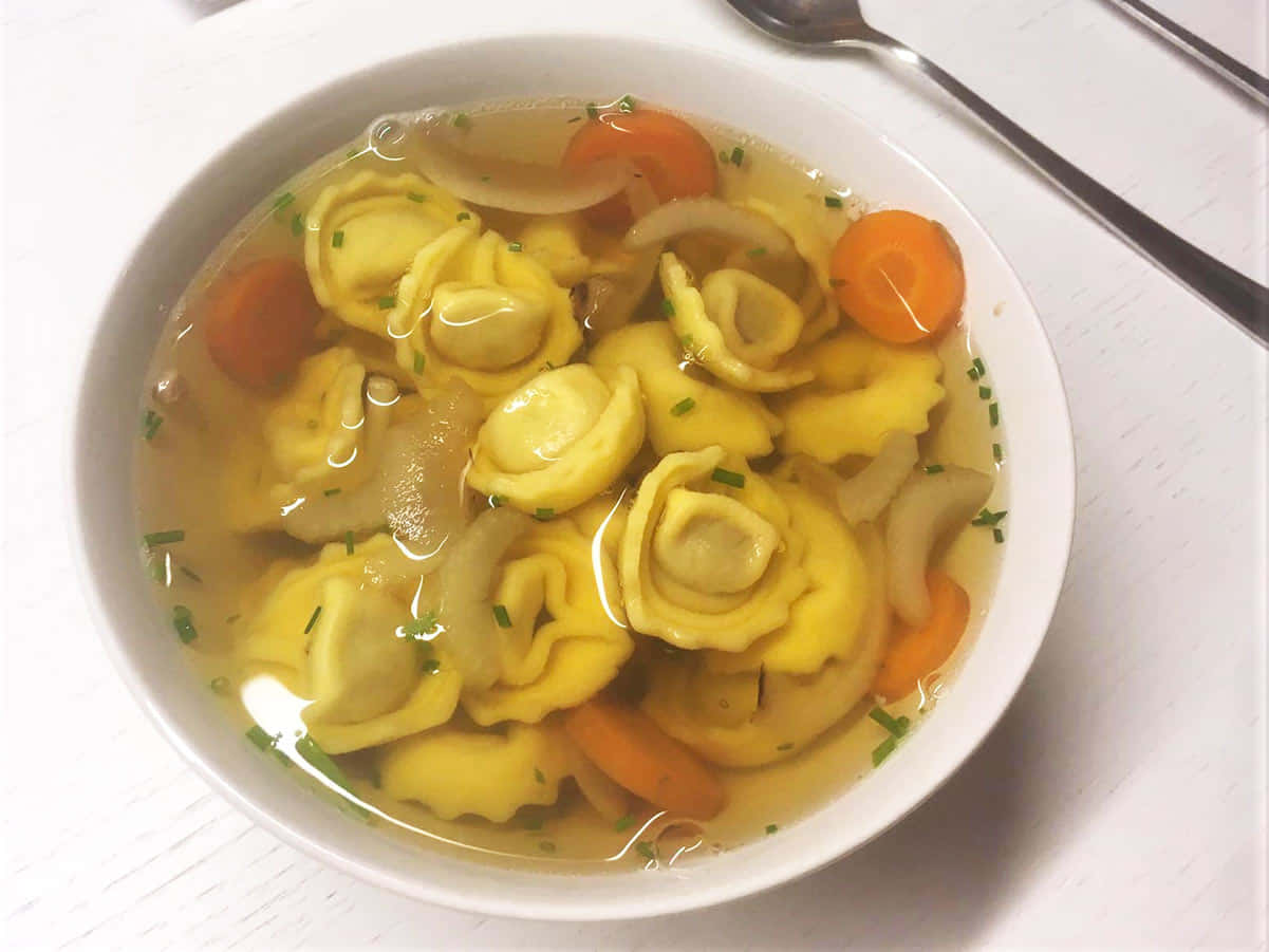 Pasta 桌布 壁紙 — 一碗熱騰騰的義大利餃子湯，配有紅蘿蔔、洋蔥和新鮮香草，清湯底。