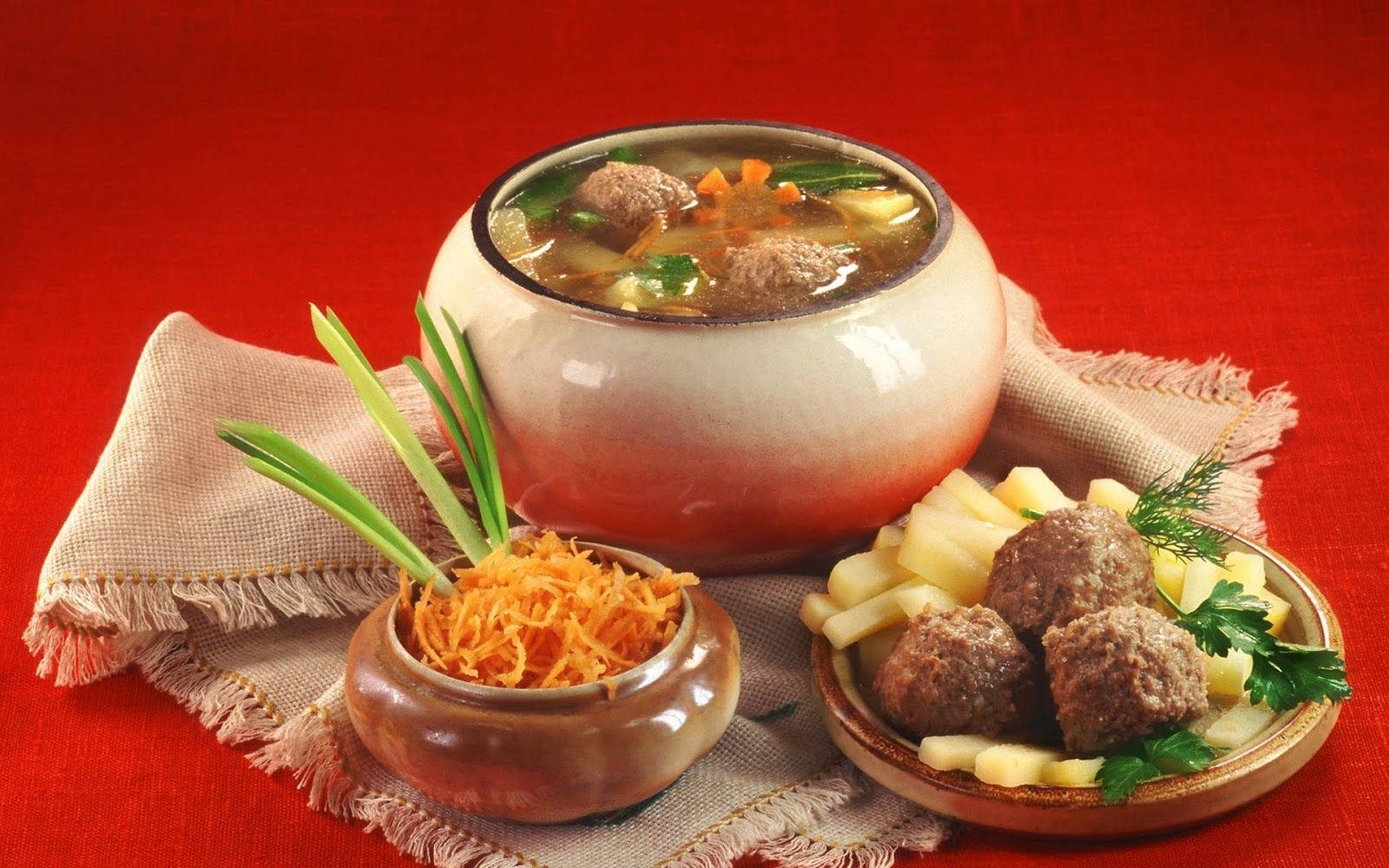 食物動圖 桌布 壁紙 — 一碗熱騰騰的豐盛肉丸湯，配有紅蘿蔔和青菜，旁邊放著一盤肉丸和切片馬鈴薯，上面撒有歐芹，放在紅色布上。