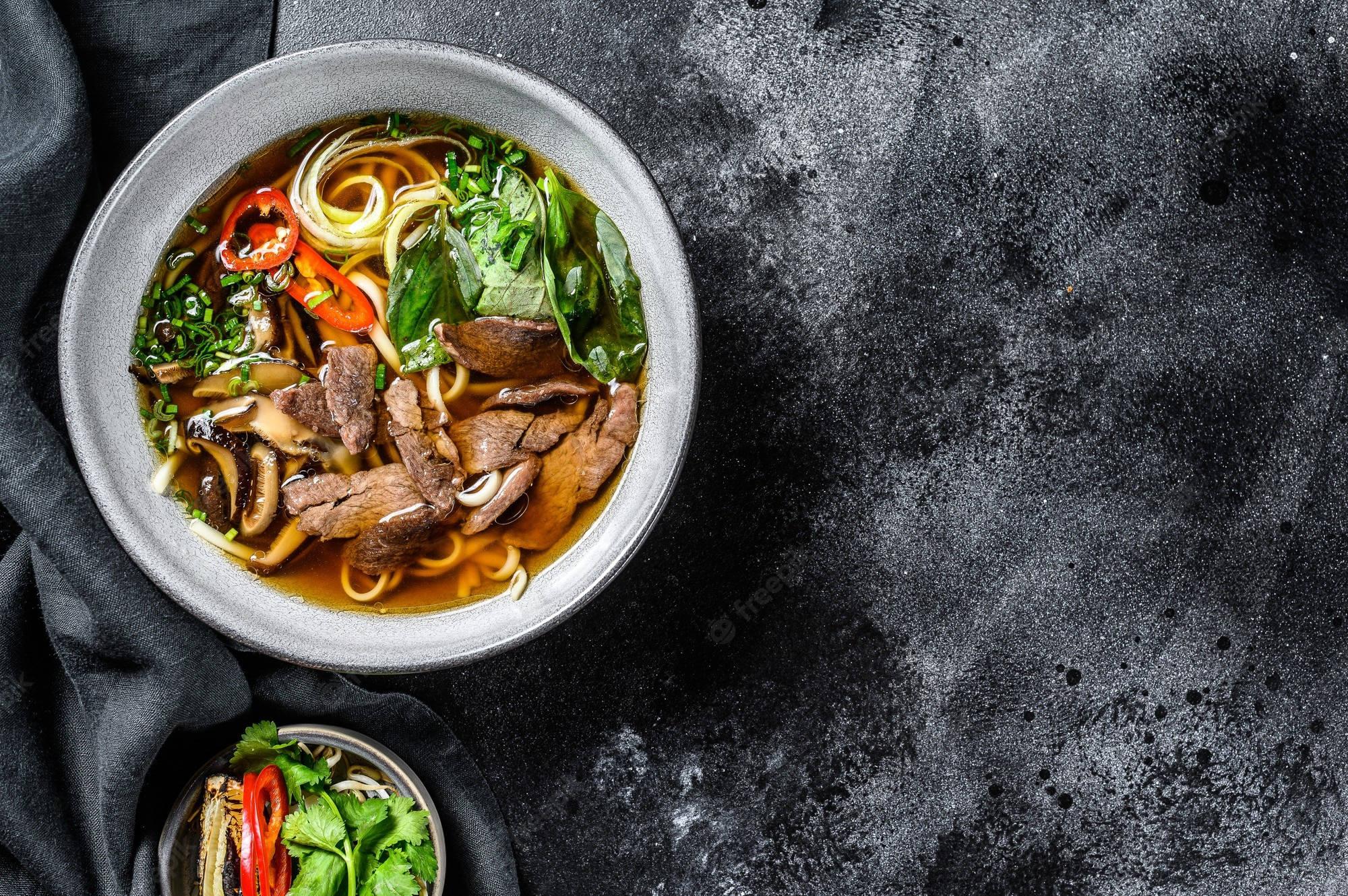 Food Photography 桌布 壁紙 — 一碗熱騰騰的越南河粉，配上嫩牛肉麵、新鮮香草和紅辣椒，放在深色紋理表面上。
