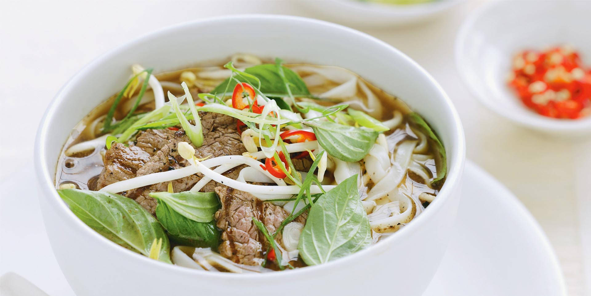 Noodles 桌布 壁紙 — 一碗熱騰騰的越南河粉，配上嫩牛肉麵、新鮮香草和紅辣椒裝飾。