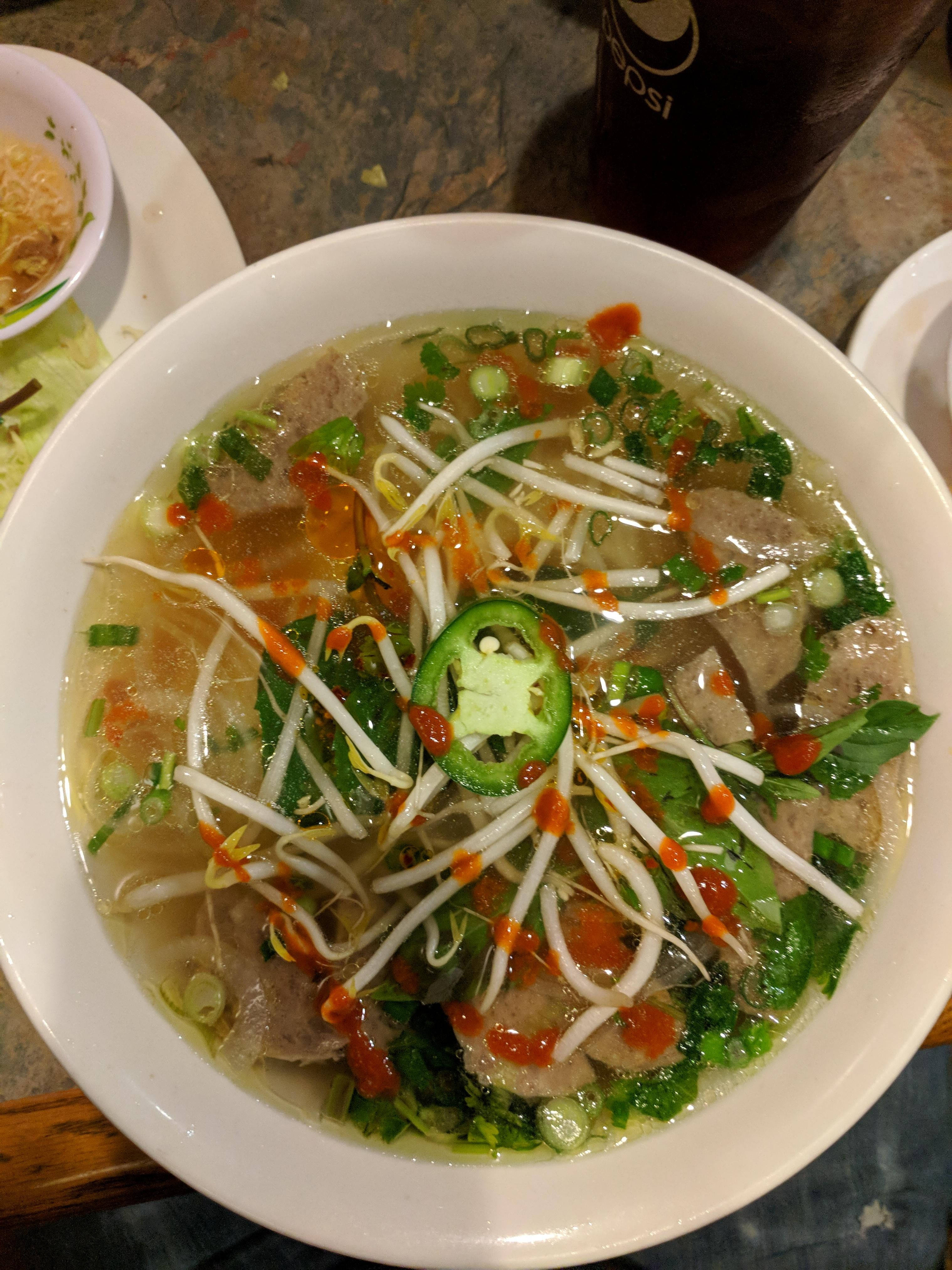 Spicy 桌布 壁紙 — 一碗熱騰騰的越南河粉，配上嫩牛肉片、豆芽、新鮮香草，以及一片鮮綠色的辣椒，並以紅辣椒油點綴。