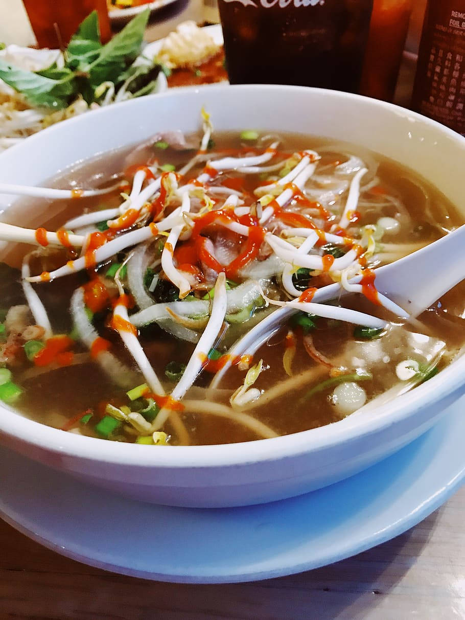 Spicy 桌布 壁紙 — 一碗熱騰騰的越南河粉，配上豆芽、洋蔥和辣椒油，放在藍色盤子上，附有湯匙，隨時可以享用。