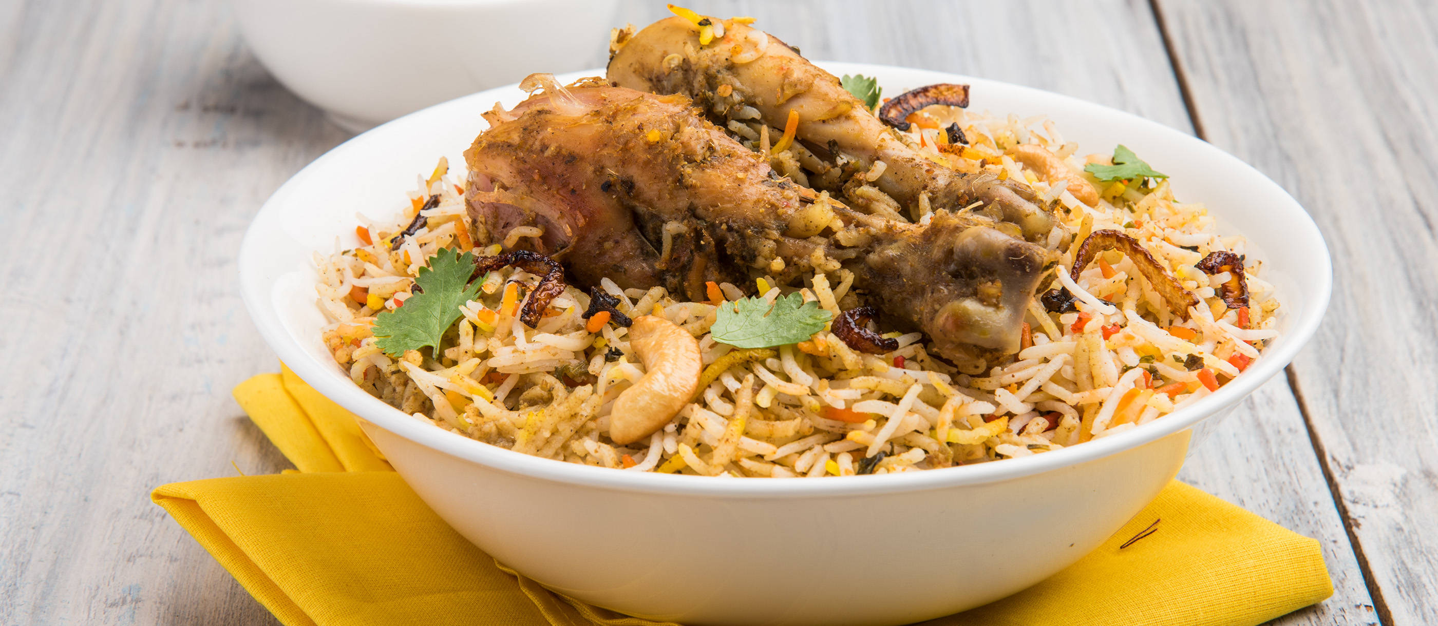 Rice 桌布 壁紙 — 一碗熱騰騰的香氣四溢雞肉印度香飯，配上腰果和香菜，放在鄉村風格木桌上的黃色餐巾上。