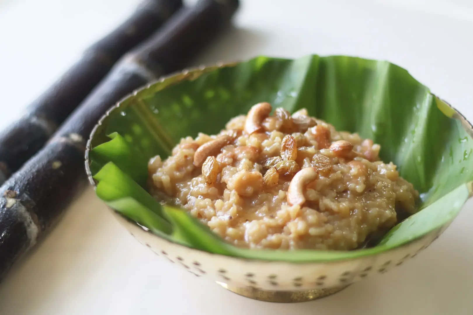 Pongal 桌布 壁紙 — 一碗甜米布丁，上面放有腰果，放在香蕉葉上，旁邊有甘蔗莖。