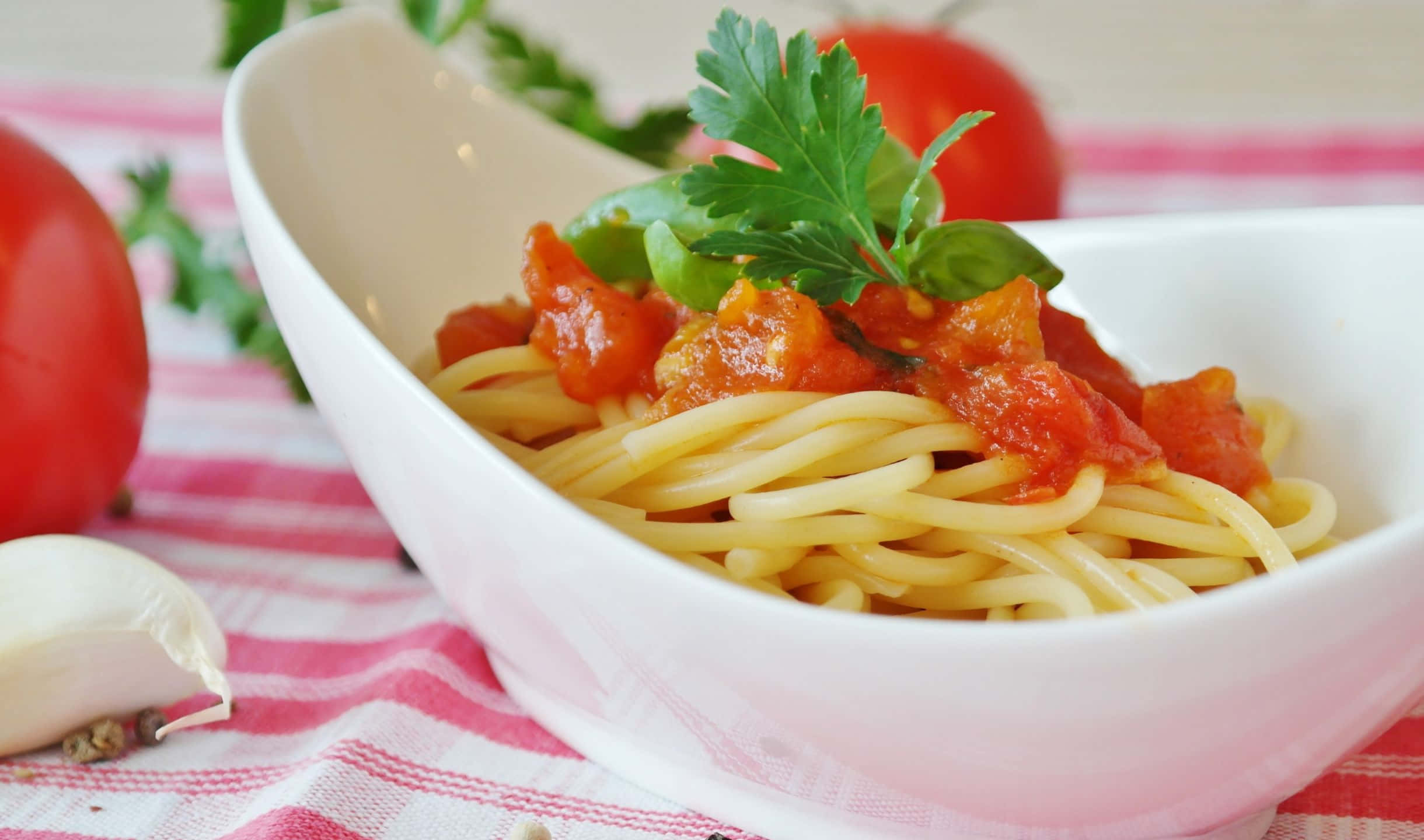 2440x1440 Pasta 桌布 壁紙 — 一碗白色義大利麵搭配濃郁番茄醬和新鮮羅勒，放在紅白格子布上，旁邊有完整番茄和大蒜。