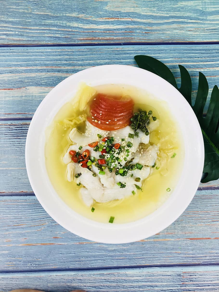 Food Photography 桌布 壁紙 — 一碗精緻魚片清湯，上面放有番茄片、切碎的辣椒和青蔥，放在一張風化的藍色木桌上。