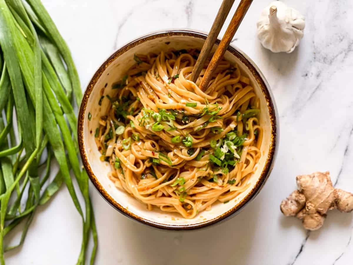 Food Photography 桌布 壁紙 — 一碗美味麵條，上面撒上切碎的青蔥，放在大理石檯面上，旁邊是新鮮大蒜和生薑。