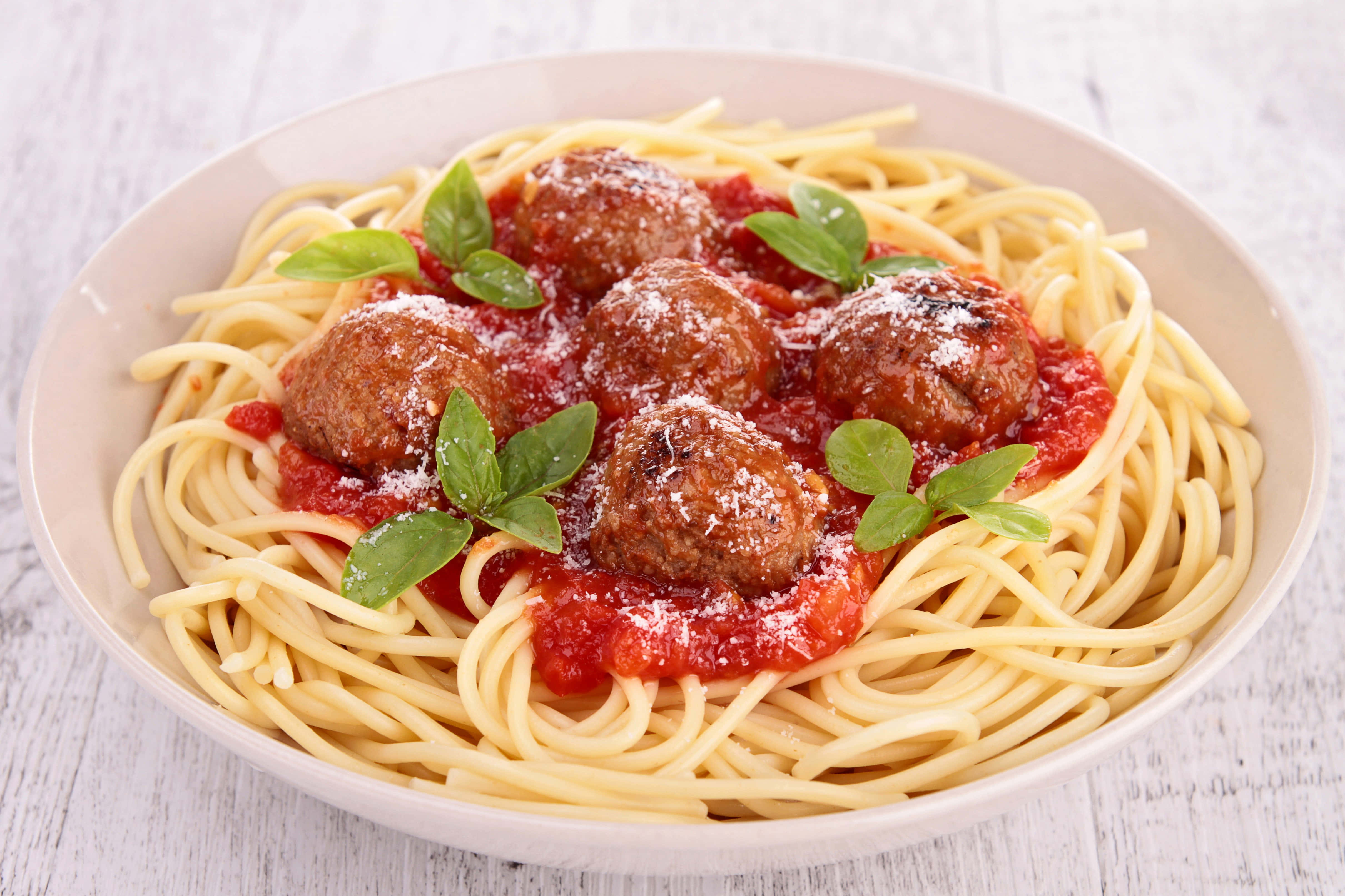 4K Pasta 桌布 壁紙 — 一碗肉丸義大利麵搭配濃郁番茄醬，飾以新鮮羅勒和磨碎起司，放在質樸的白色木桌上。