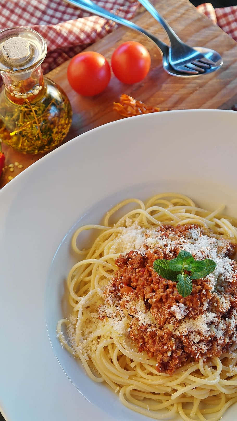 Spaghetti 桌布 壁紙 — 一碗肉醬義大利麵，上面撒有磨碎的起司和新鮮薄荷，放在木板上，旁邊有櫻桃番茄和橄欖油。