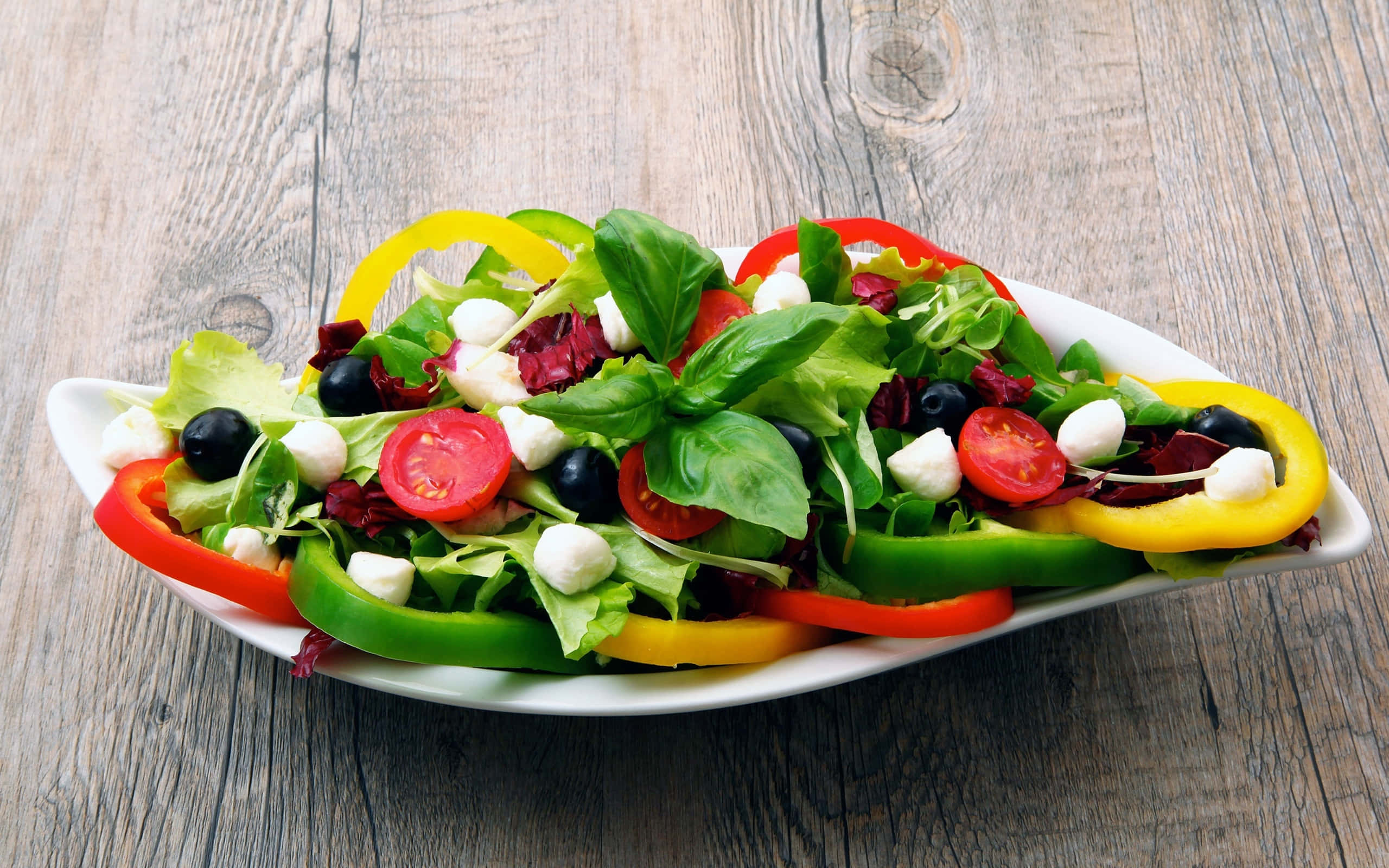 沙拉 桌布 壁紙 — 一碗色彩繽紛的新鮮沙拉，有櫻桃番茄、橄欖、莫札瑞拉起司和彩色甜椒，放在白色碗中，置於鄉村風木桌上。