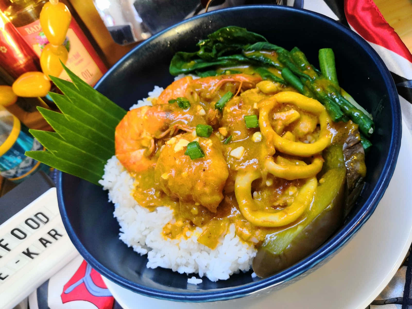 Delicious Food 桌布 壁紙 — 一碗色彩繽紛的泰式咖哩，配上蝦、魷魚和青菜，放在白飯上，並以青蔥和香蕉葉點綴。