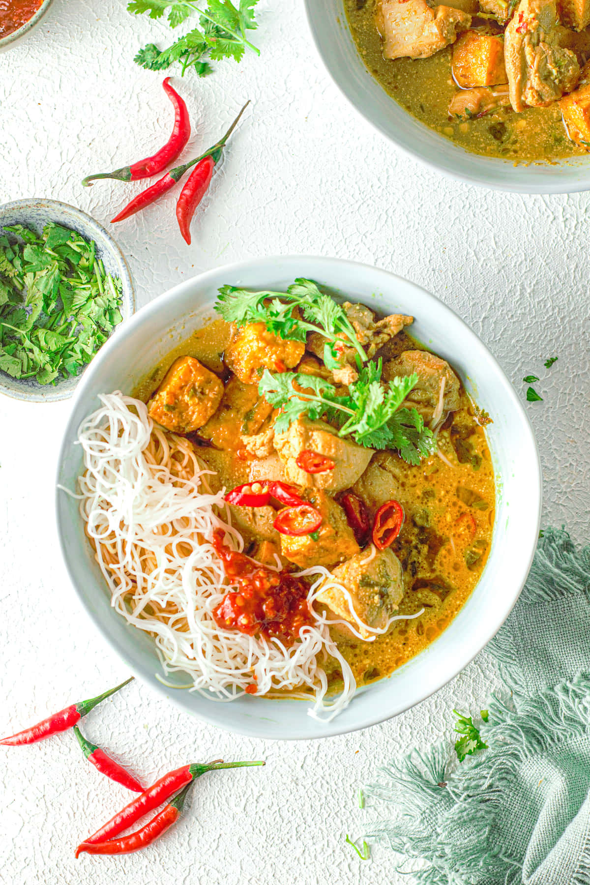 Noodles 桌布 壁紙 — 一碗色彩繽紛的泰式咖哩，配上麵條、雞肉和新鮮香菜，並以紅辣椒點綴，置於有紋理的白色表面上。