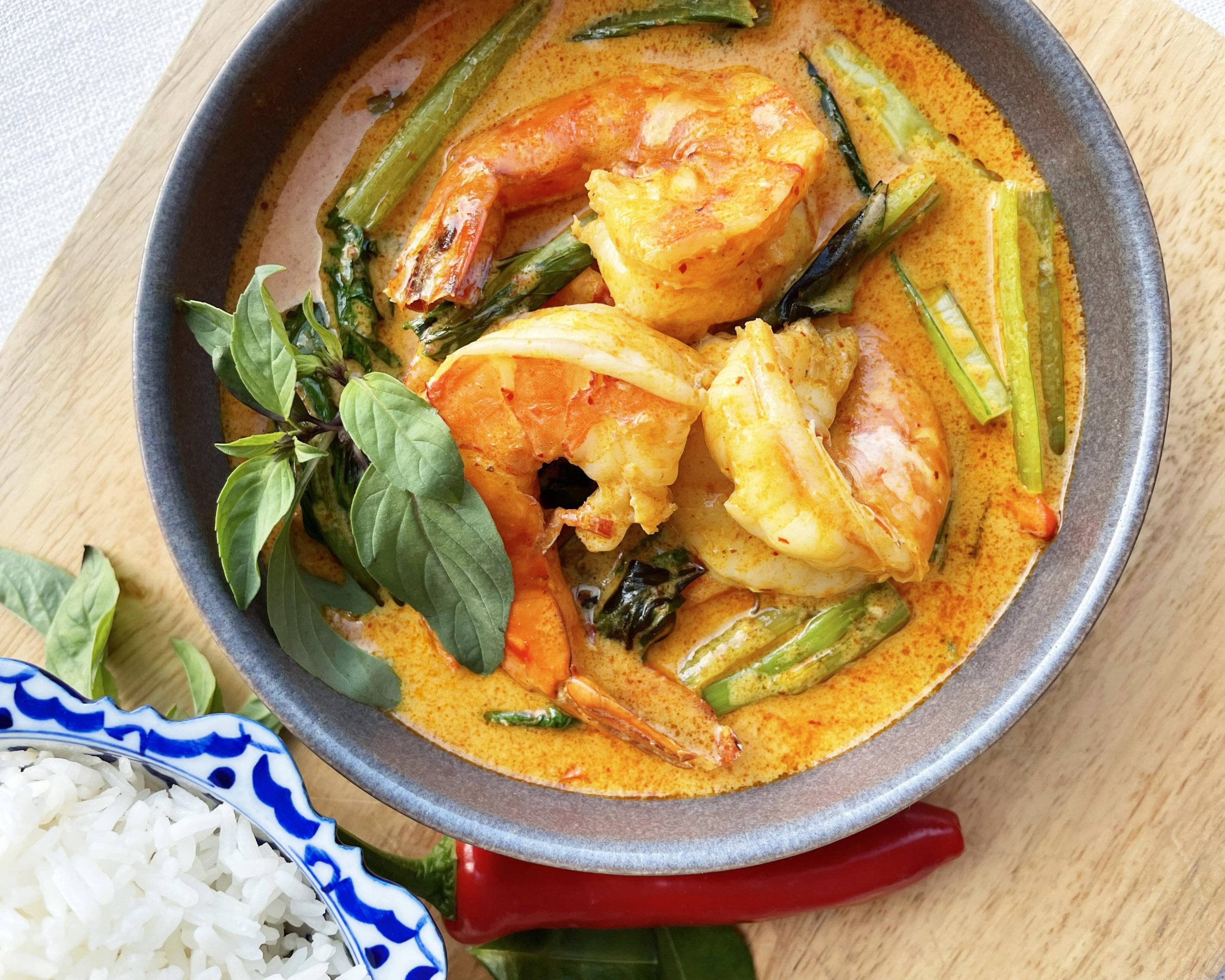 Delicious Food 桌布 壁紙 — 一碗色彩繽紛的泰式紅咖哩，配上多汁蝦仁、青豆和新鮮羅勒，與白飯一起放在木板上享用。