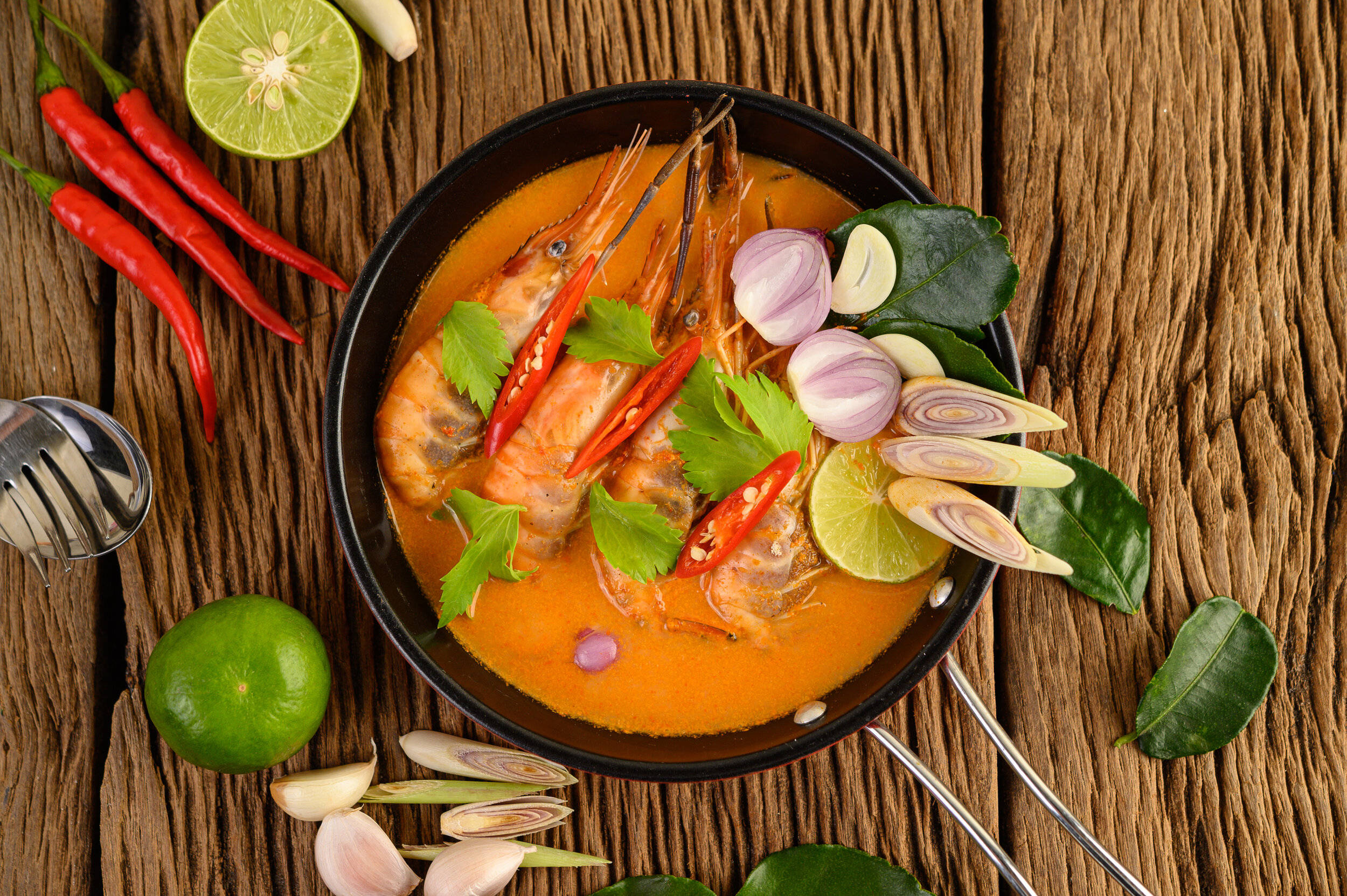 Prawns 桌布 壁紙 — 一碗色彩繽紛的泰式蝦咖哩，飾以青檸、辣椒、紅蔥頭和香草，放在質樸的木桌上。
