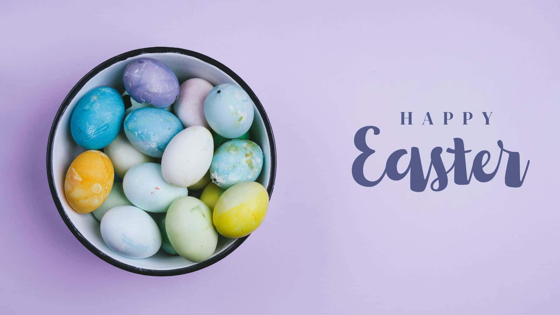 Happy Easter 桌布 壁紙 — 一碗色彩繽紛的粉彩復活節蛋放在柔和的薰衣草背景上，旁邊是優雅的手寫字體 'Happy Easter'。