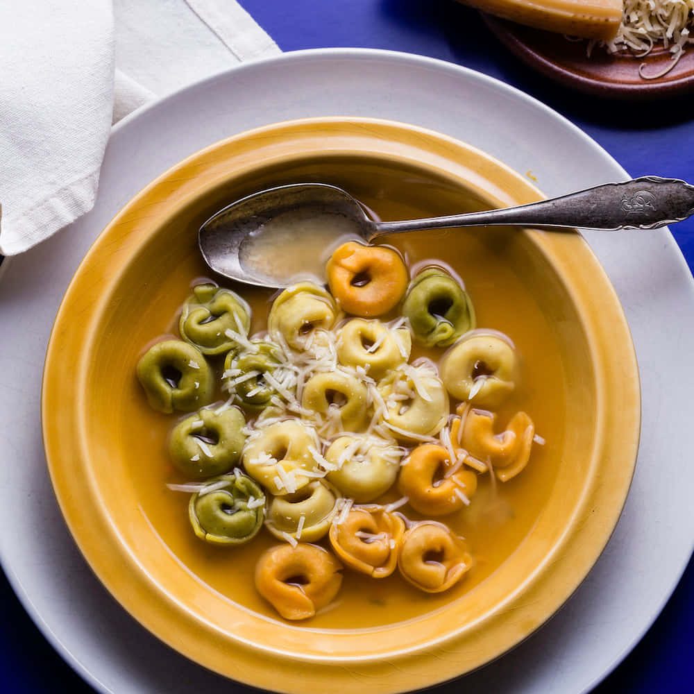 Food Photography 桌布 壁紙 — 一碗色彩繽紛的義大利餃子，配上金黃色湯汁，灑上磨碎的起司，並放有一把古董湯匙。