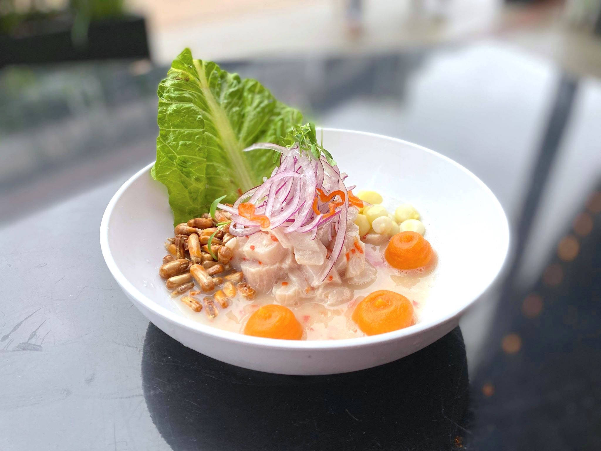 bowl 桌布 壁紙 — 一碗色彩繽紛的酸橘汁醃魚，飾以紅洋蔥、玉米和生菜，放在深色反光桌上。