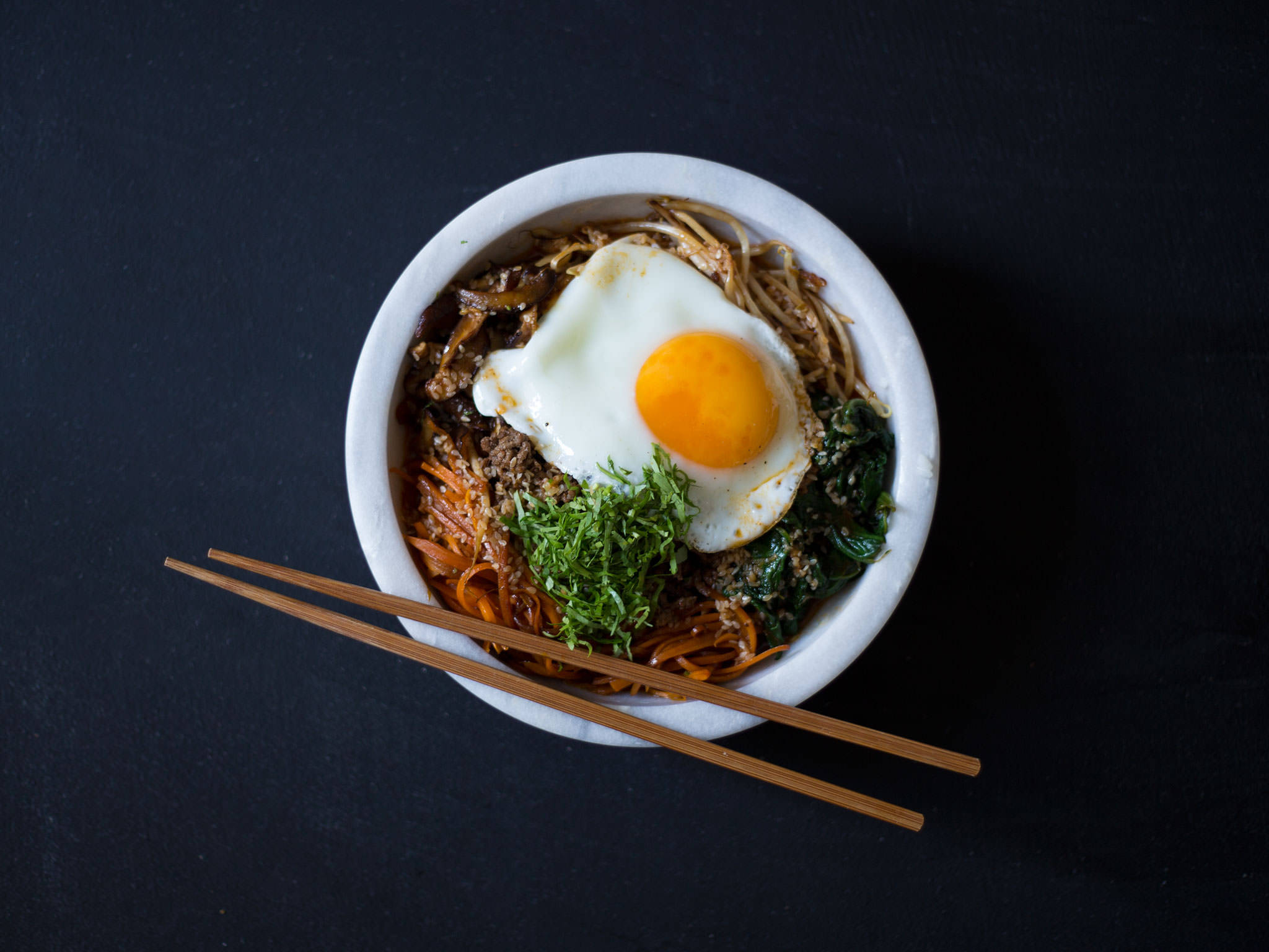 烹飪 桌布 壁紙 — 一碗色彩繽紛的韓國拌飯，上面放著太陽蛋和新鮮蔬菜，背景為深色。