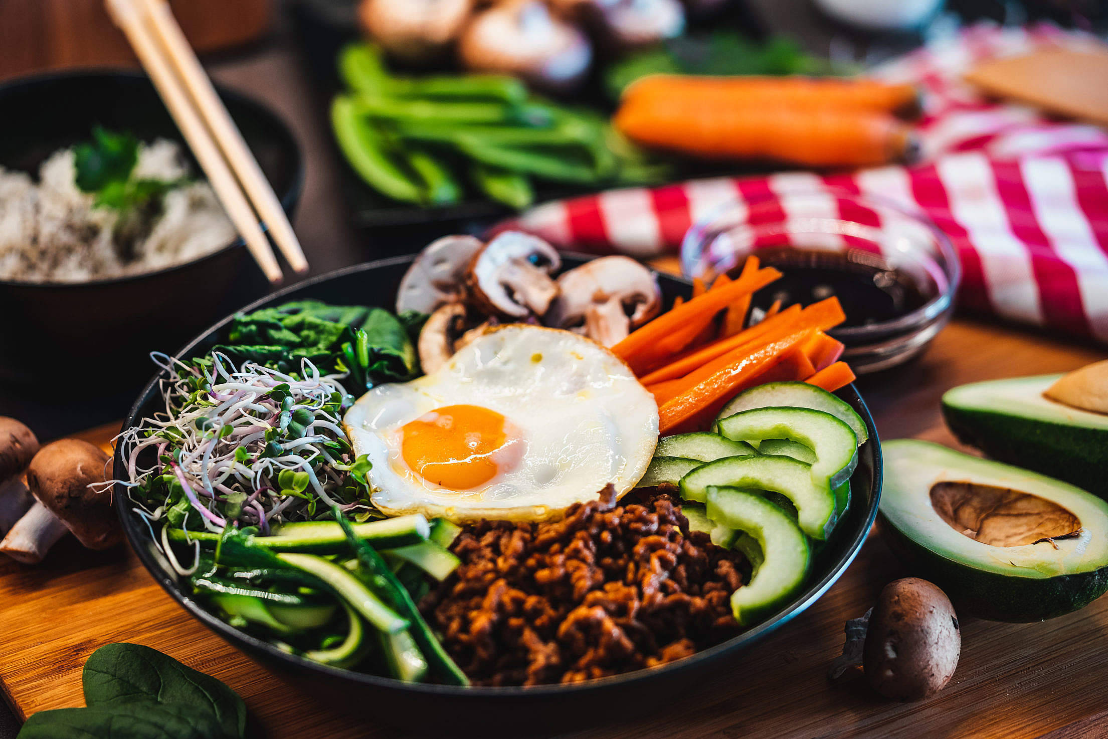 烹飪 桌布 壁紙 — 一碗色彩繽紛的韓國石鍋拌飯，上面放著太陽蛋和新鮮蔬菜，置於木桌上。