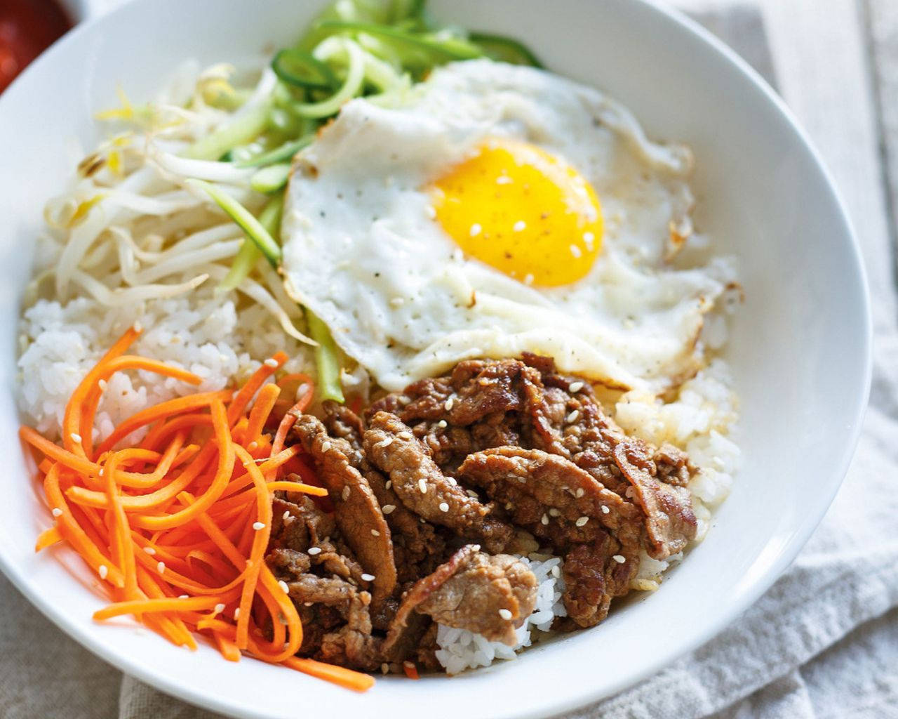 烹飪 桌布 壁紙 — 一碗色彩繽紛的韓國石鍋拌飯，上面放有太陽蛋、豆芽、紅蘿蔔和調味牛肉，搭配白飯。