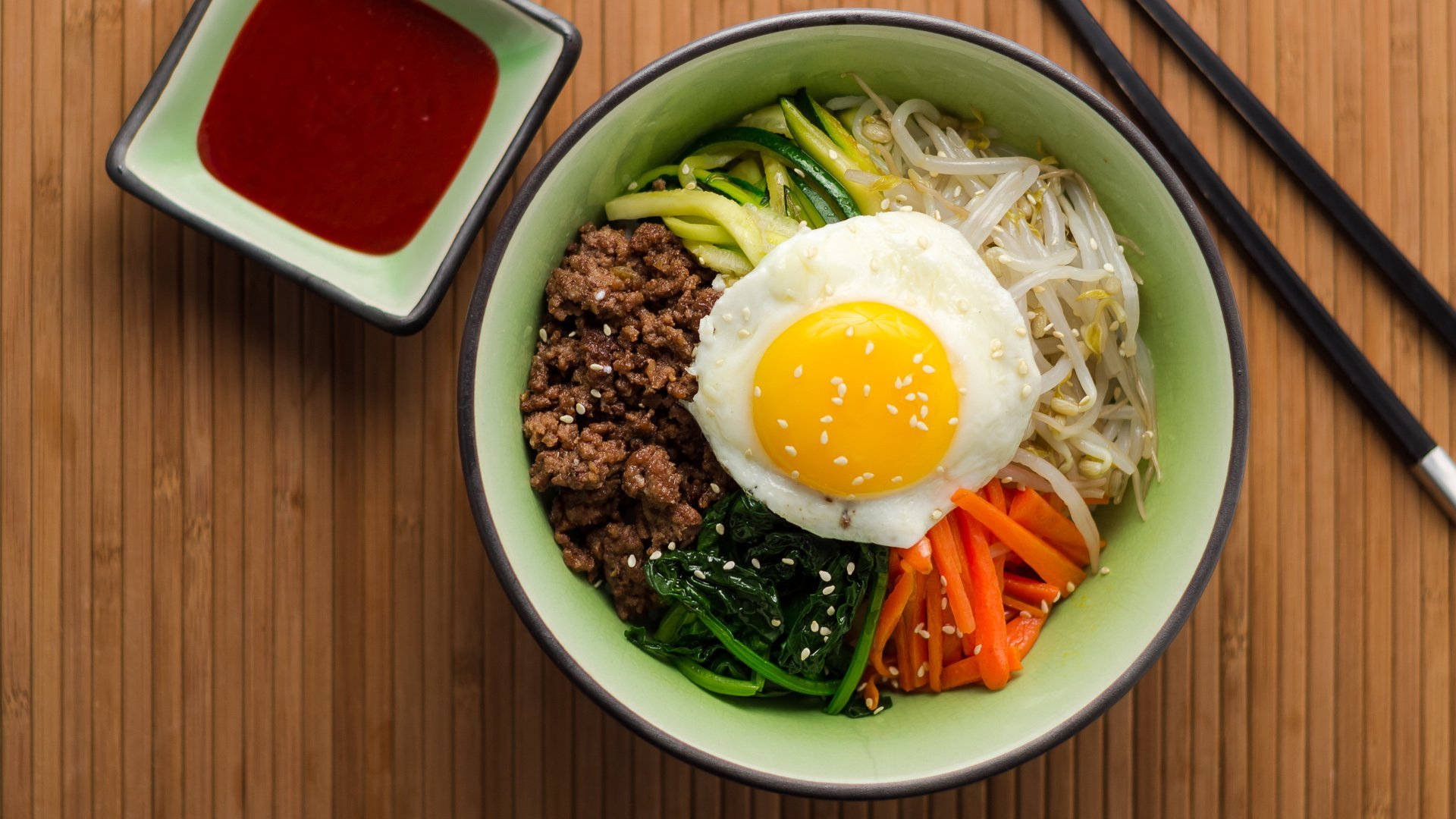 烹飪 桌布 壁紙 — 一碗色彩繽紛的韓國石鍋拌飯，上面放著太陽蛋和五顏六色的蔬菜，放在木桌上。