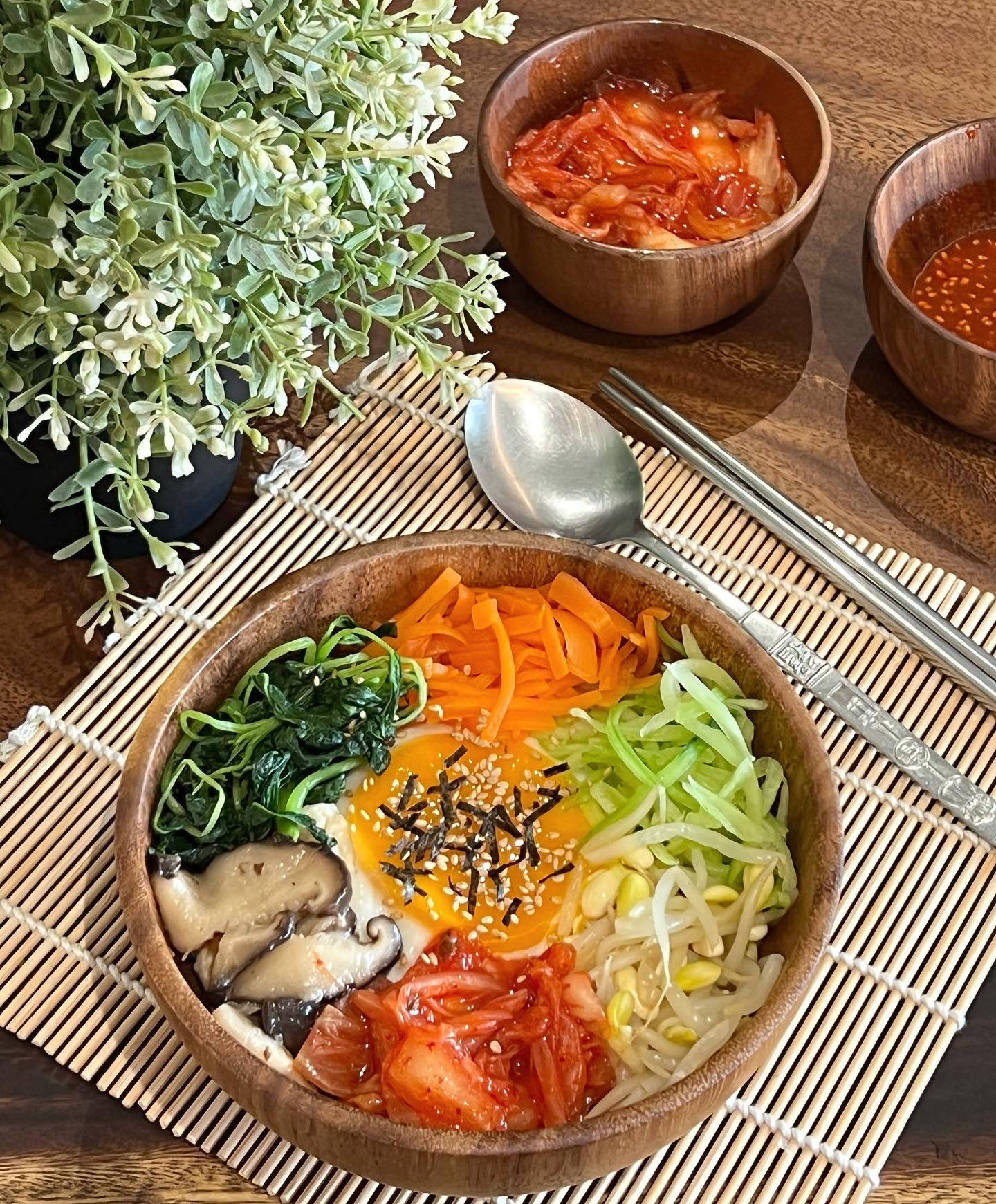 烹飪 桌布 壁紙 — 一碗色彩繽紛的韓國石鍋拌飯，配上各色蔬菜、芝麻和太陽蛋，放在竹蓆上，旁邊有泡菜和筷子。